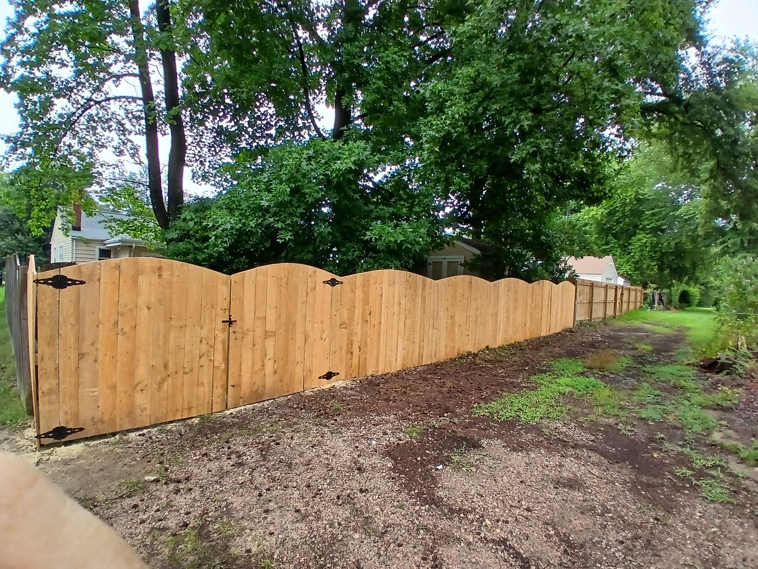 New wooden privacy fence along a yard with green trees and a gravel pathway.