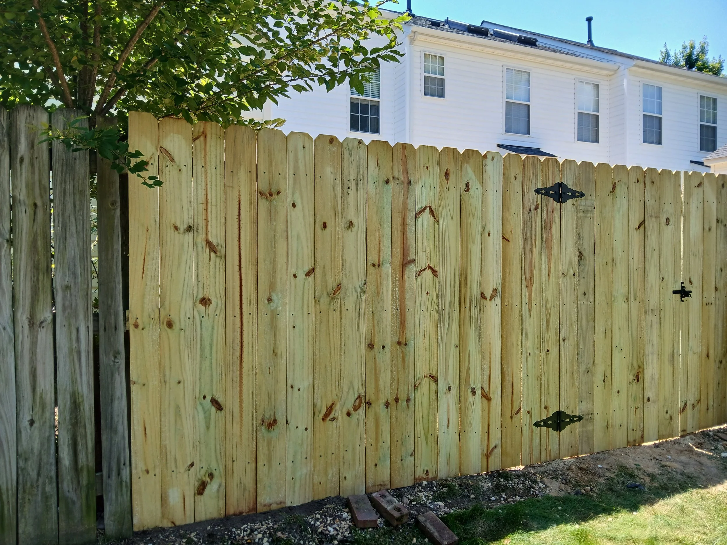 New wooden picket fence with hinges and latch in front of a white residential building with multiple windows.