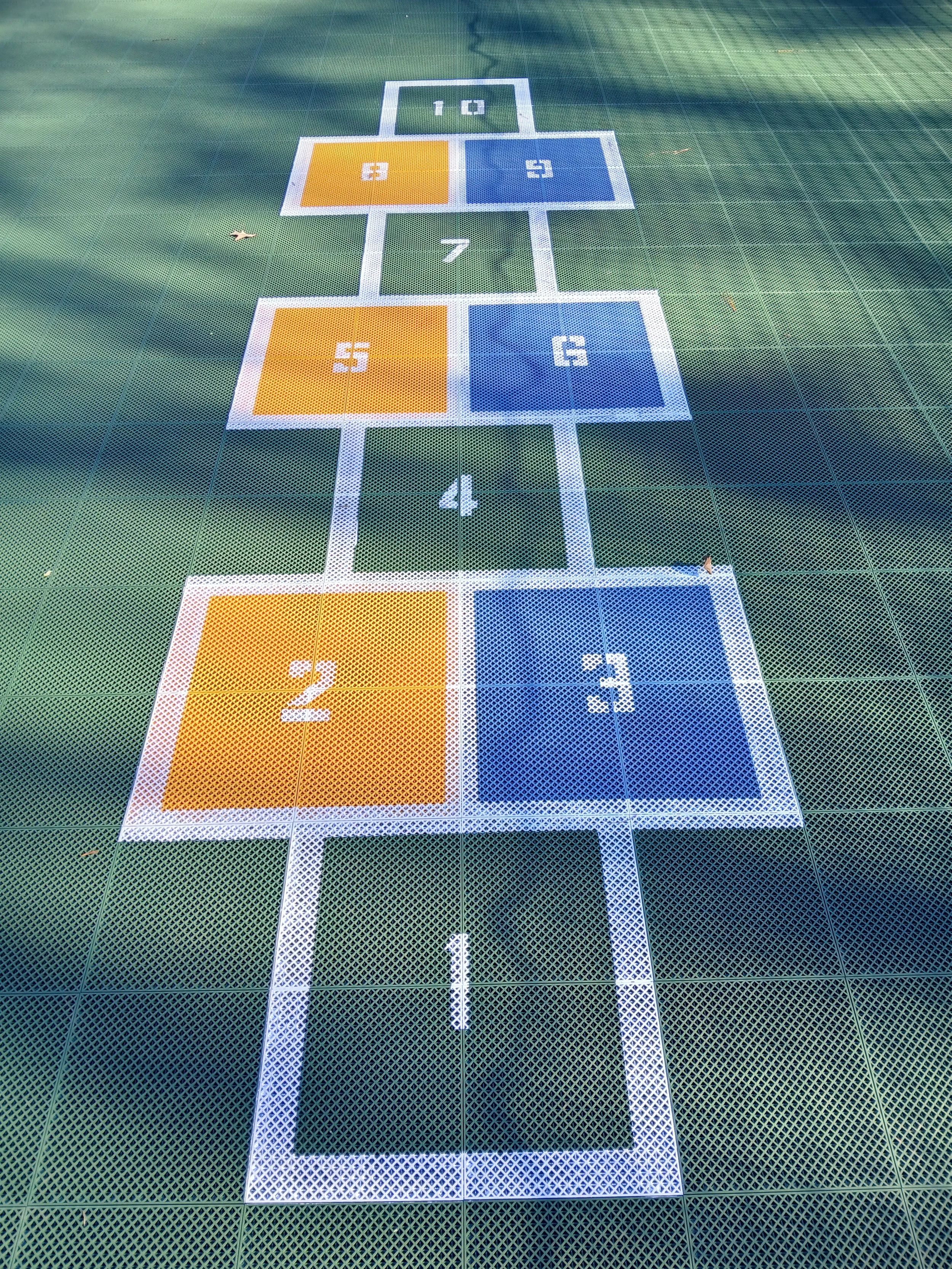 Colorful outdoor hopscotch court with numbered squares from 1 to 10 arranged in a traditional pattern on a green surface.