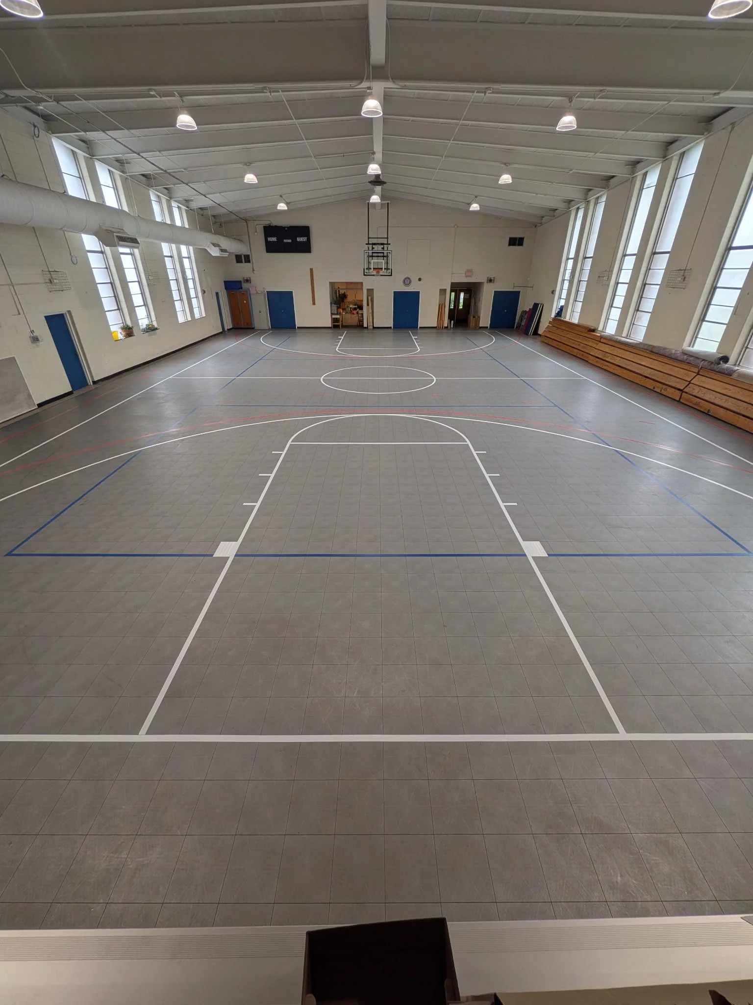 Empty indoor basketball court with a scoreboard, basketball hoop, and benches along the side.