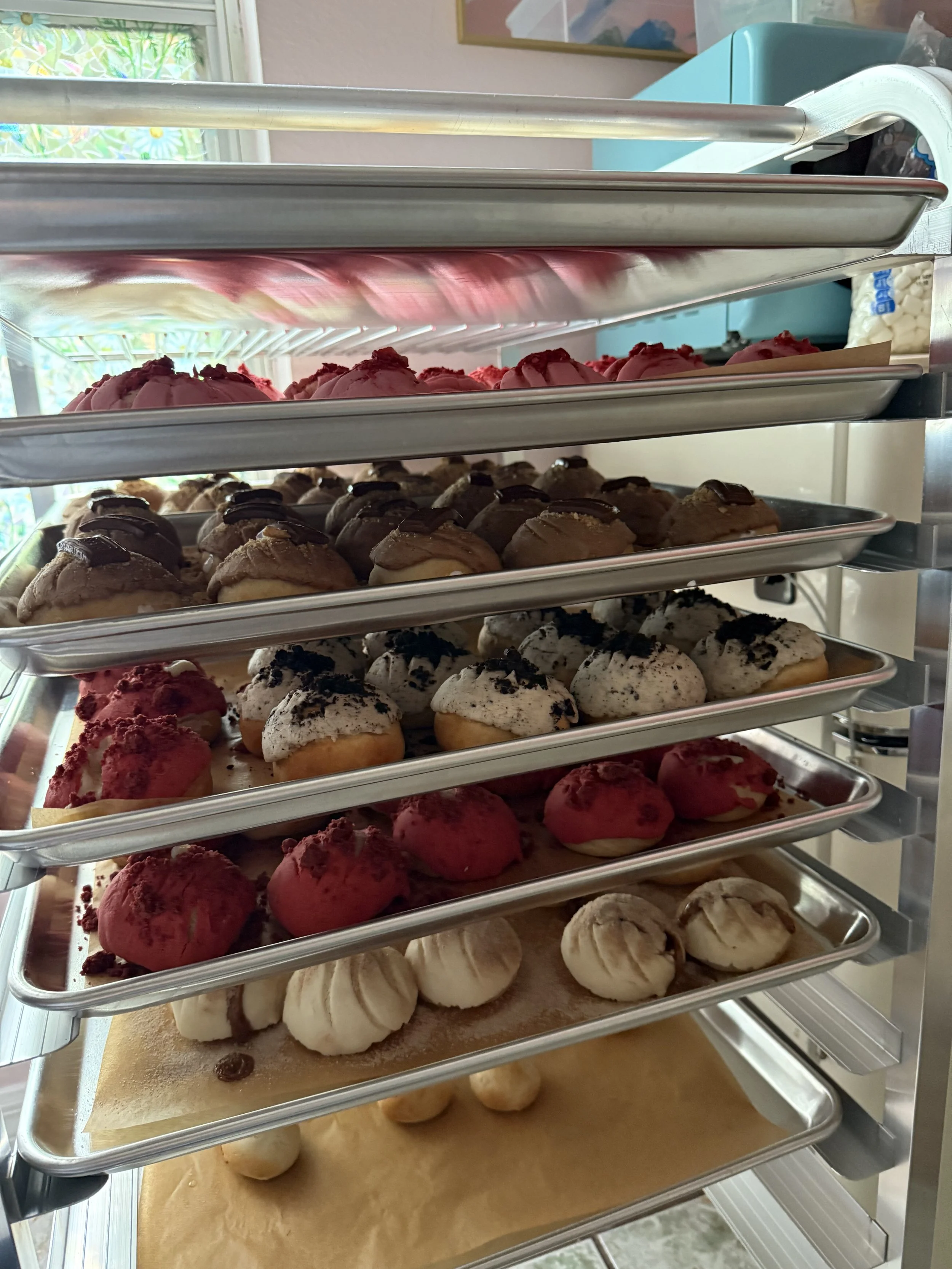 A display case with multiple shelves filled with various types of colorful cookies and pastries, including pink, brown, black and white, and beige cookies.