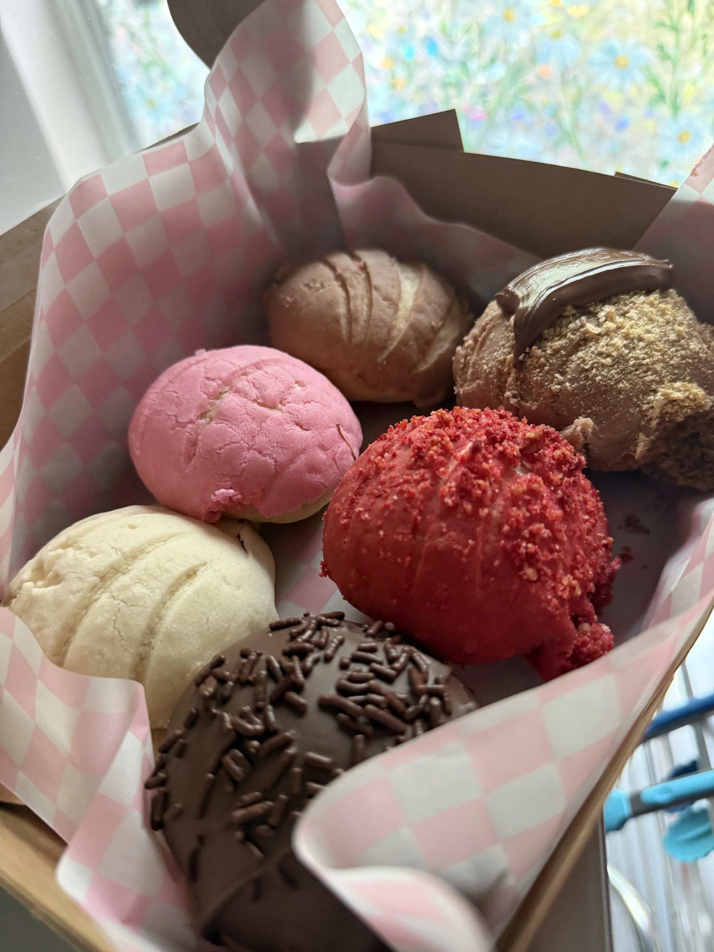 A box of assorted colorful cookies including pink, white, red, brown, and chocolate-covered cookies with sprinkles.