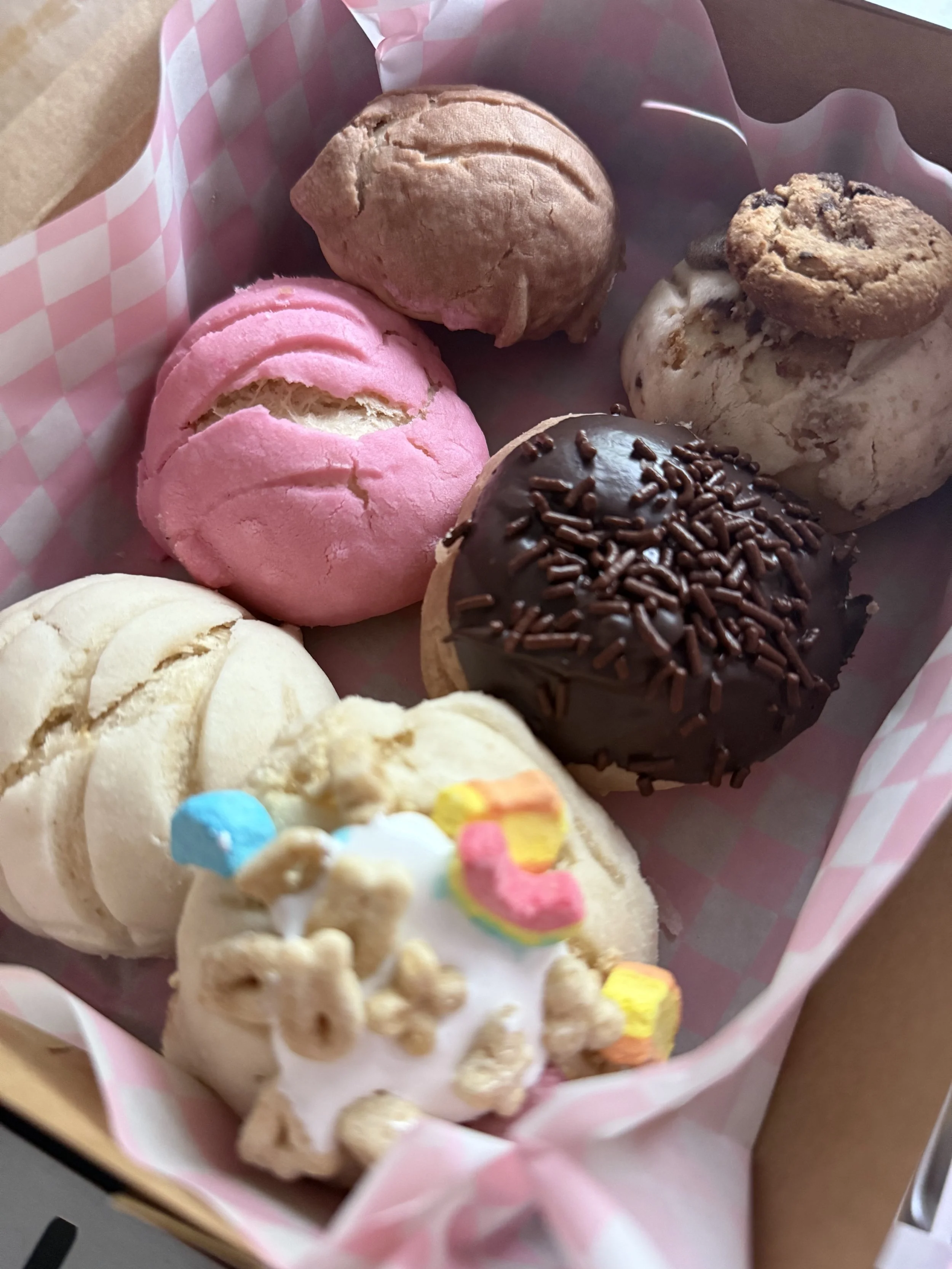 A pink, white, and brown basket of assorted cookies, including chocolate-dipped, frosted, and decorated sugar cookies.