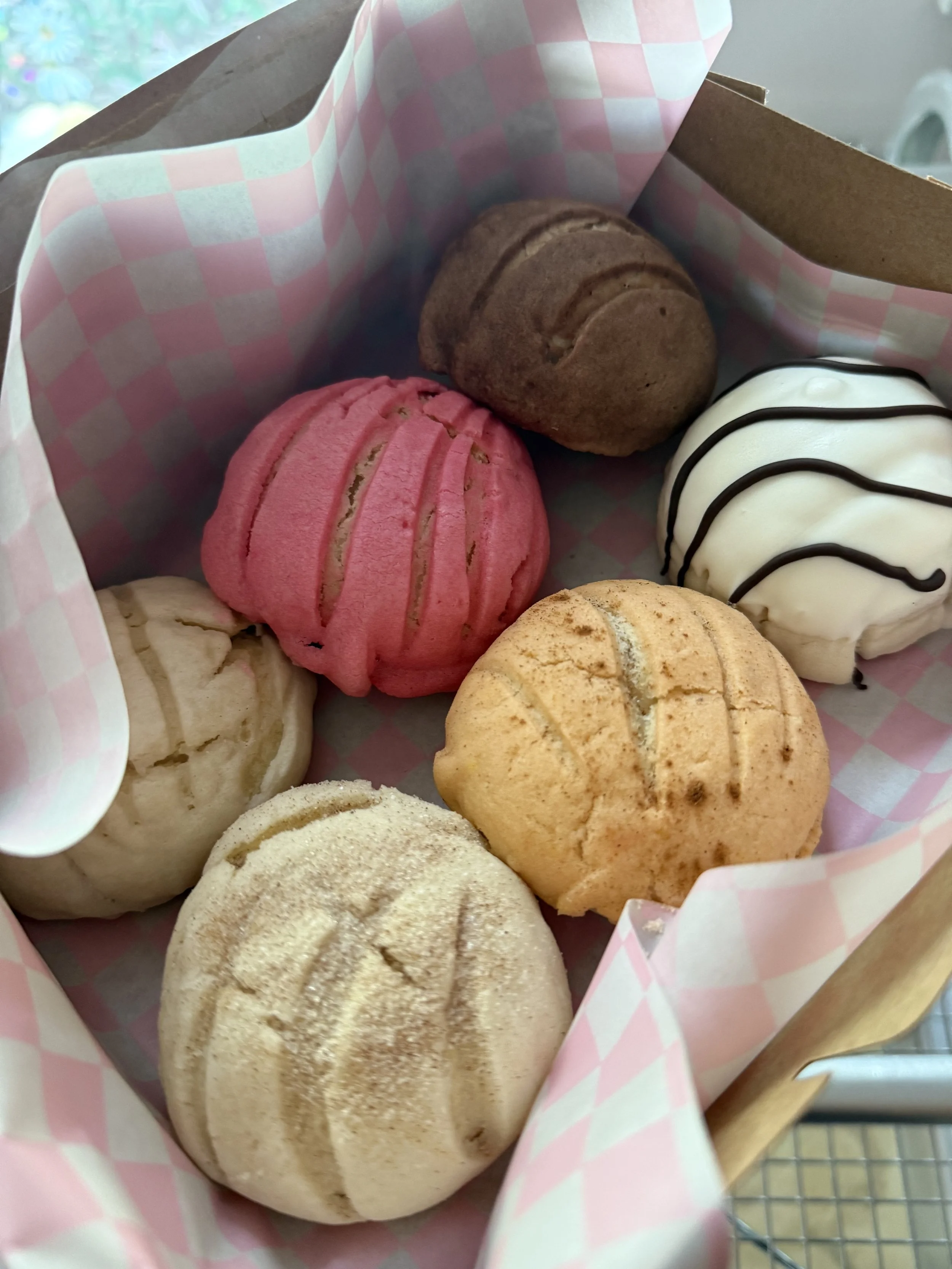 A basket with six colorful steamed buns with various toppings and fillings, lined with pink and white checkered paper.