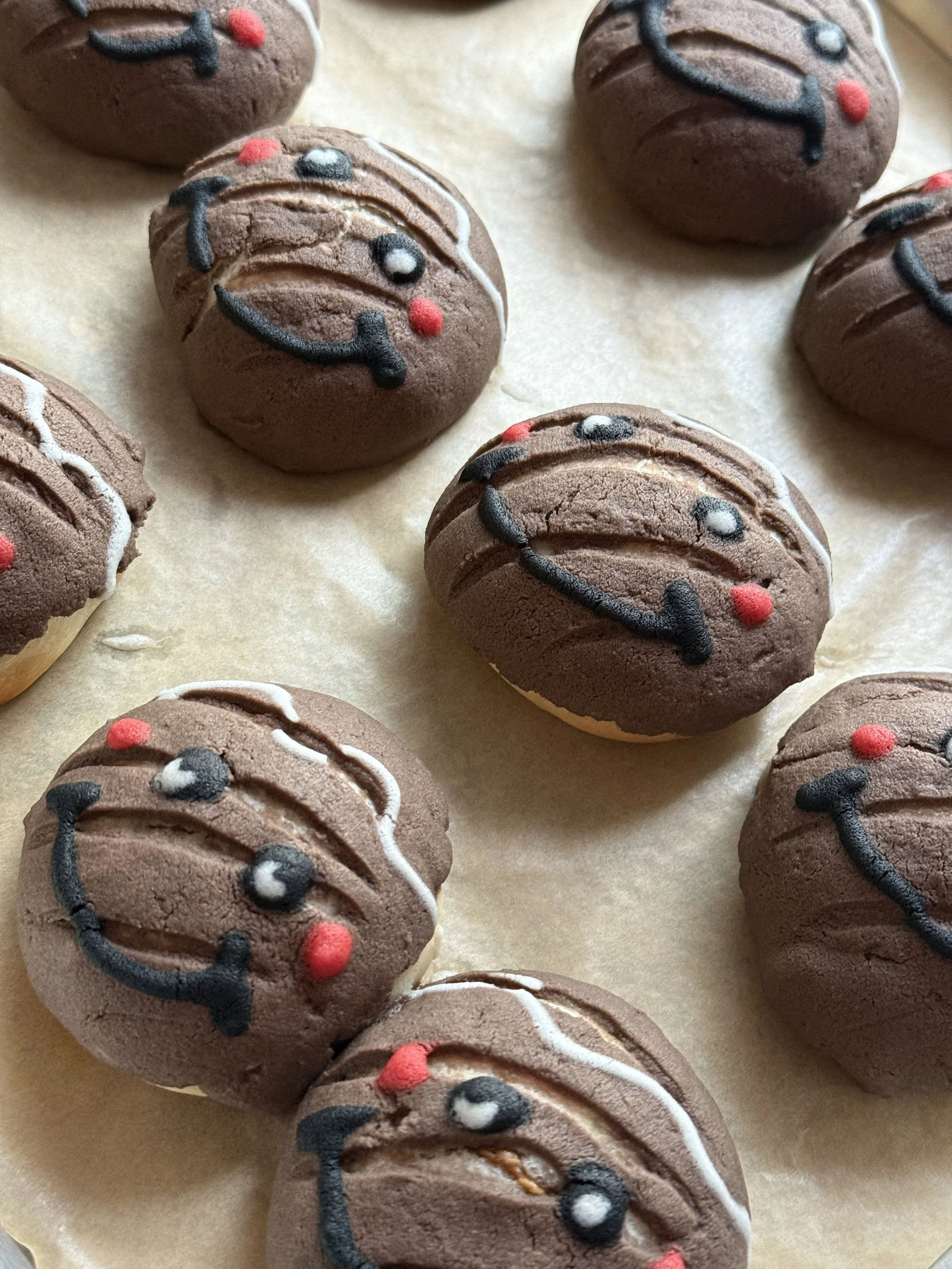 Chocolate cookies decorated with icing to look like reindeers, with red noses and smiling expressions.