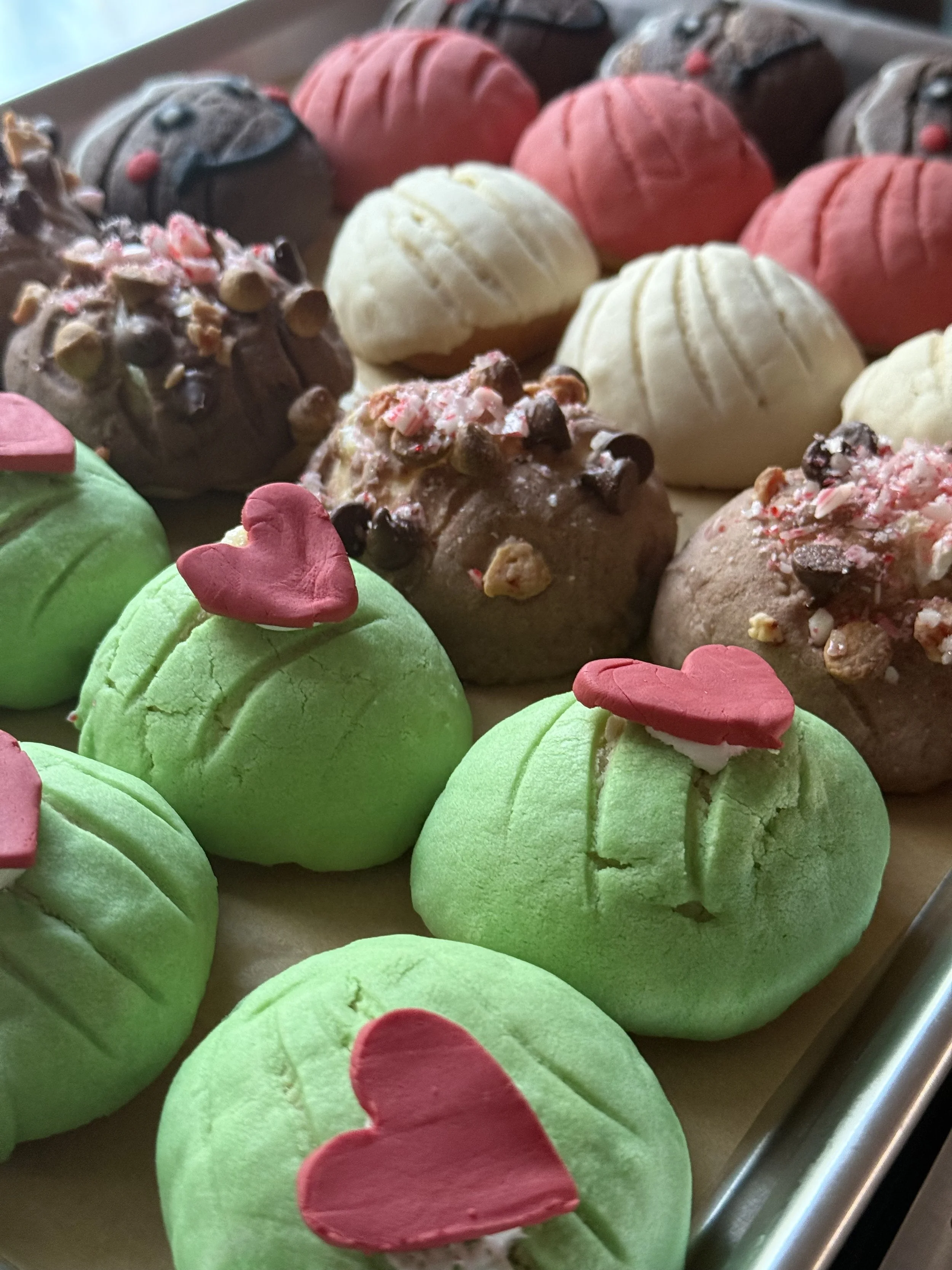 Close-up of decorated macaron and truffle confections with pink and red heart and flower toppers on a tray.