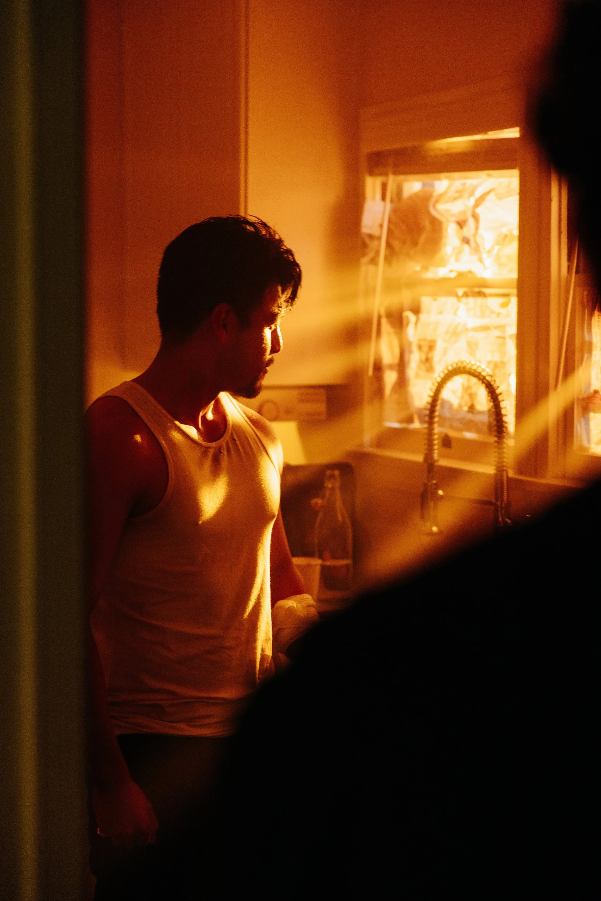 A man standing in a kitchen, illuminated by warm sunlight coming through the window, with a focused expression. From the short film Kentucky Bourbon 2026.
