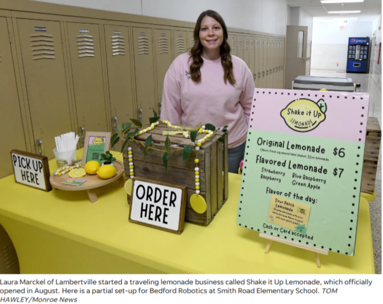 Shake It Up Lemonade founder pictured behind her setup at Smith Road Elementary Temperance Michigan as featured  Monroe News article “Former teacher shakes up her career”