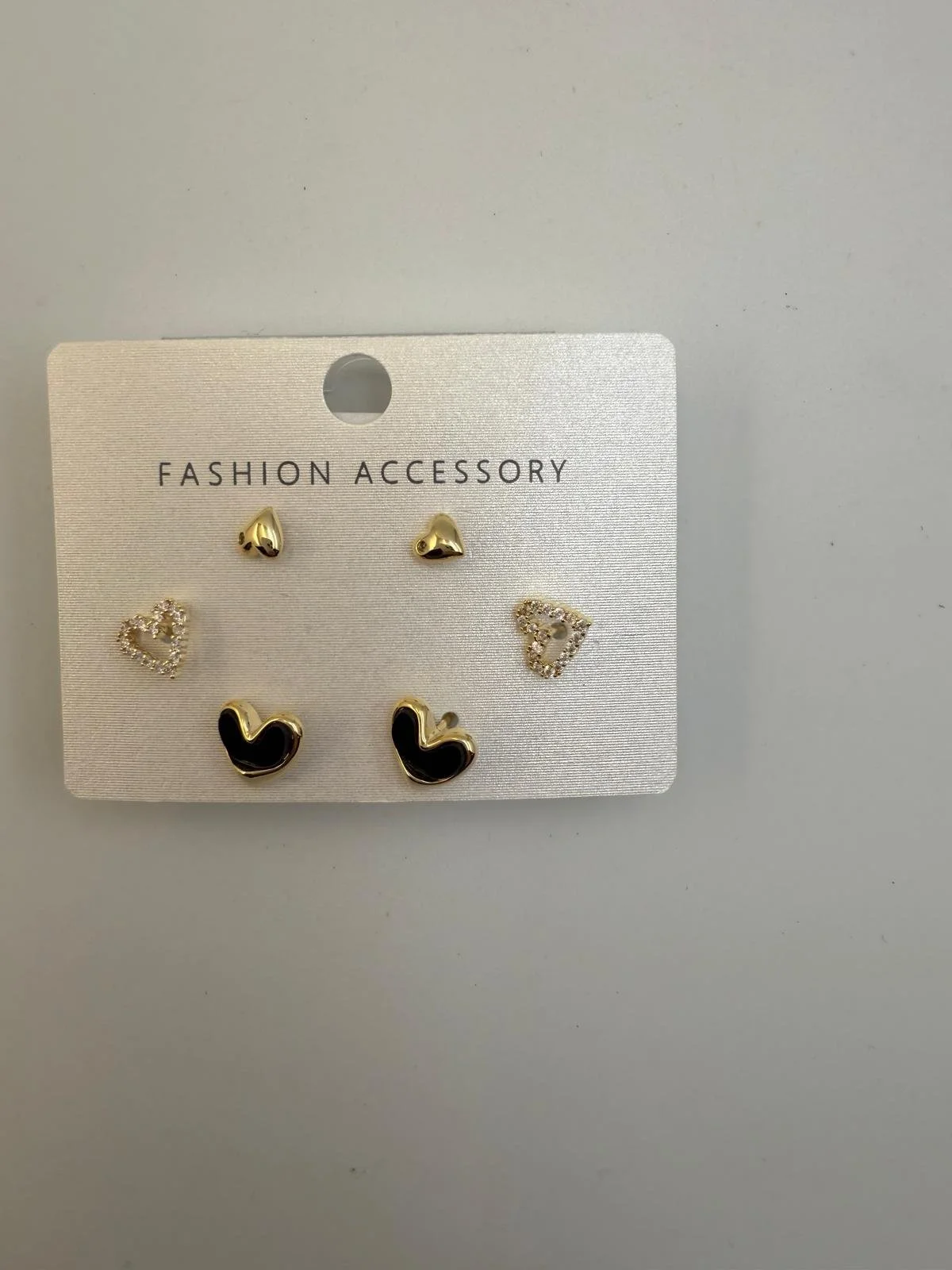 Set of six earrings on a white card labeled "Fashion Accessory". The earrings include small gold heart-shaped studs, clear rhinestone hearts, and black and gold hearts.