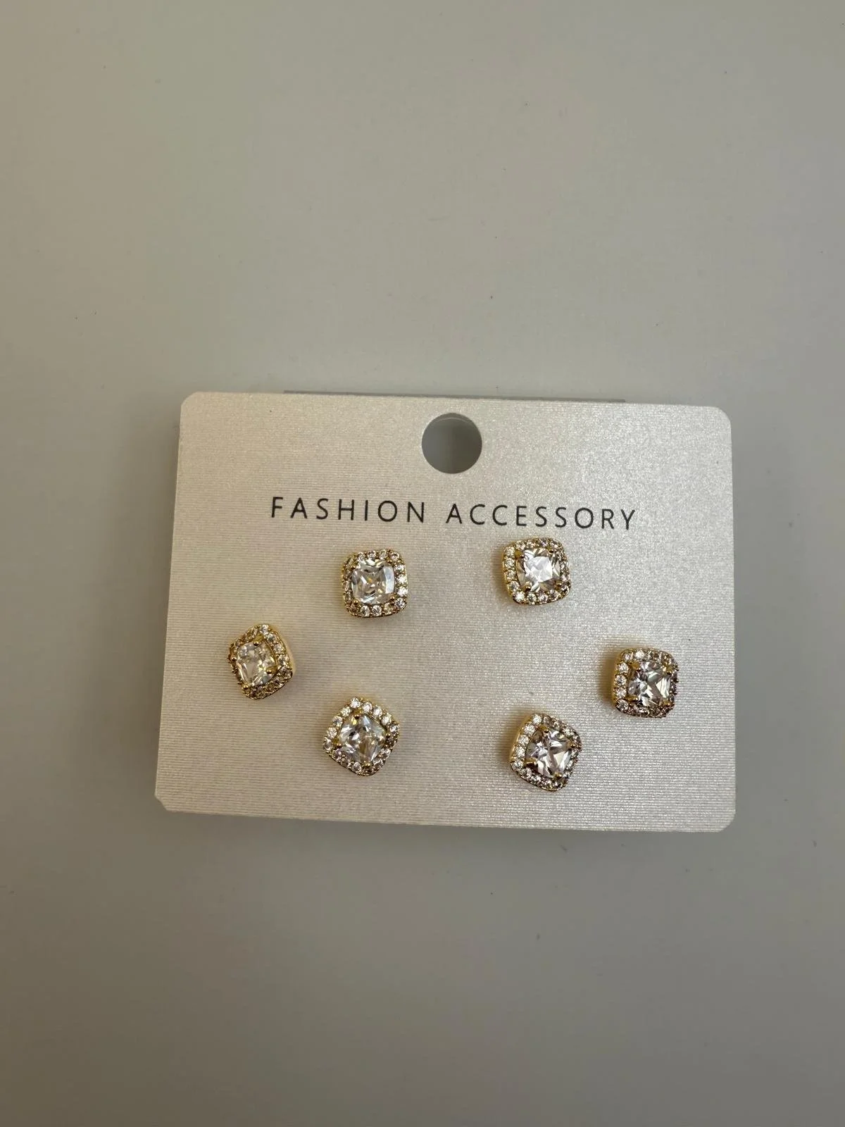 Set of six square earrings with clear central stones surrounded by smaller stones on a white card labeled "Fashion Accessory".