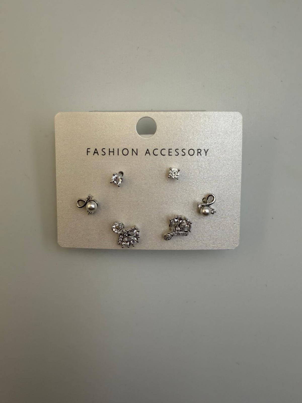 Stud earrings on a card labeled 'Fashion Accessory', including a pair of small diamond studs, pearl earrings with a bow design, and decorative earrings with crystals.