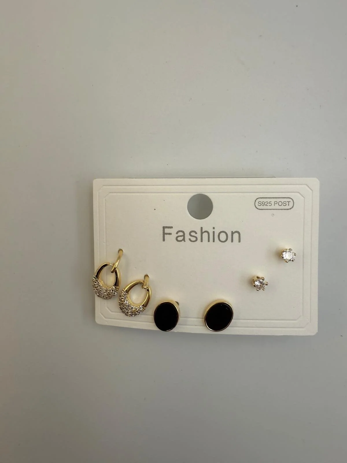 Display card with four pairs of earrings, including gold hoops with rhinestones, black stone studs, and clear rhinestone studs, labeled 'Fashion'.