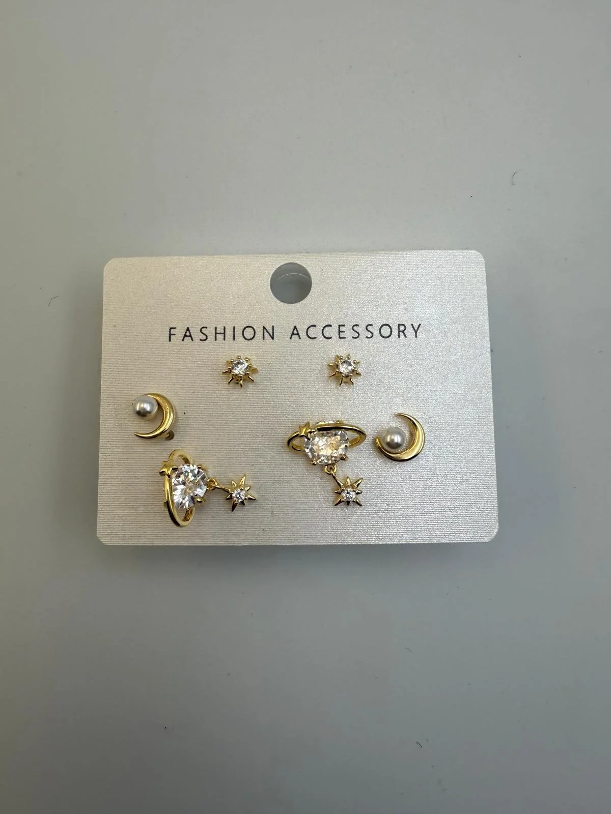 Set of six gold and silver earrings with star and moon shapes, some with small pearls and clear stones, on a white card labeled 'Fashion Accessory'.