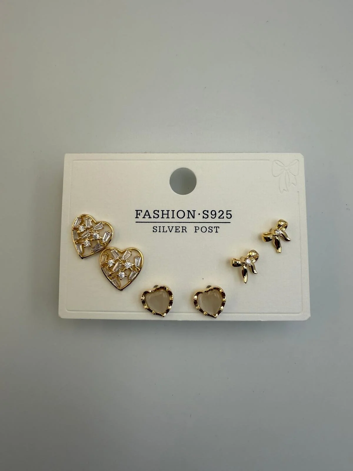 A white card with gold and silver heart-shaped earrings with rhinestones displayed on it.