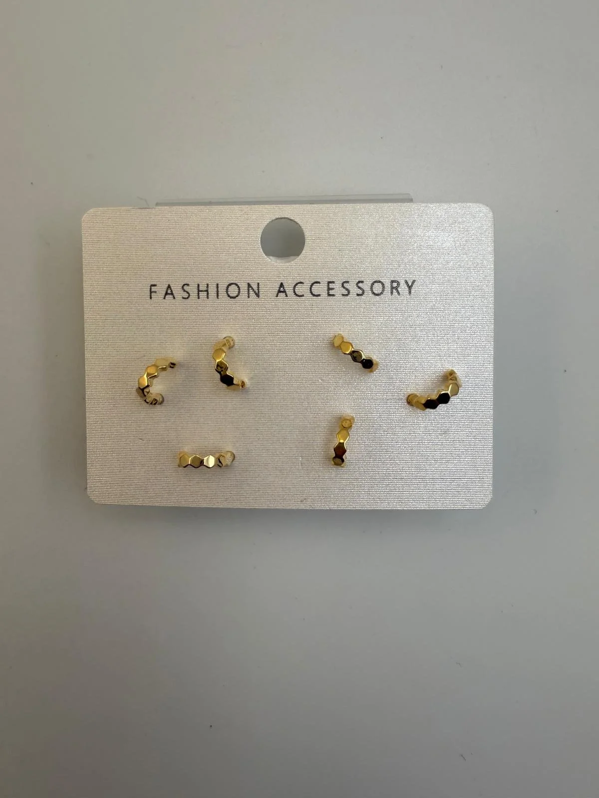 Set of five small gold-colored hexagon-shaped earrings on a white card labeled "Fashion Accessory".