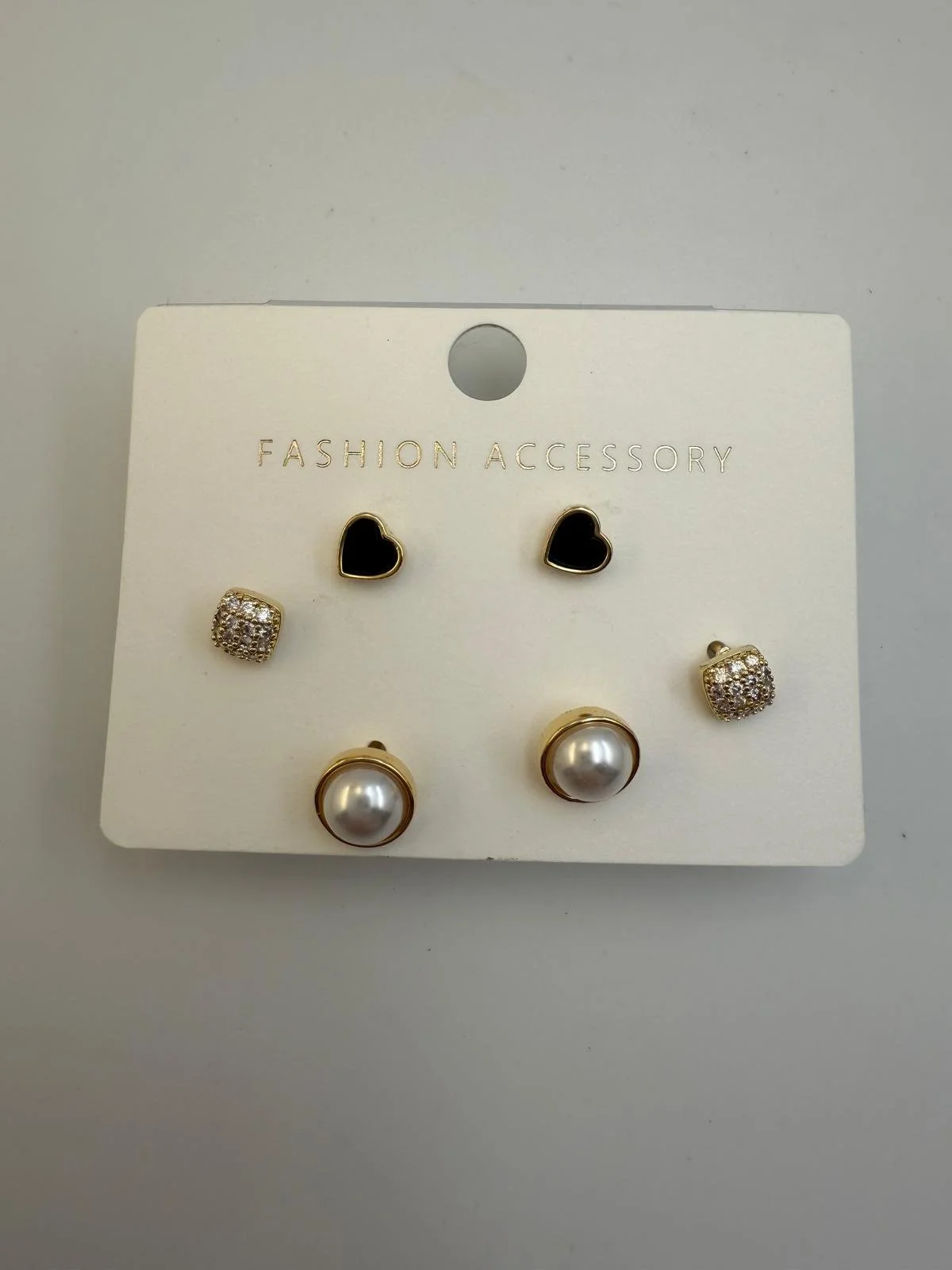 Set of four pairs of earrings on a white display card labeled "Fashion Accessory." The earrings include black heart-shaped studs, clear rhinestone square studs, and large pearl studs with gold trim.