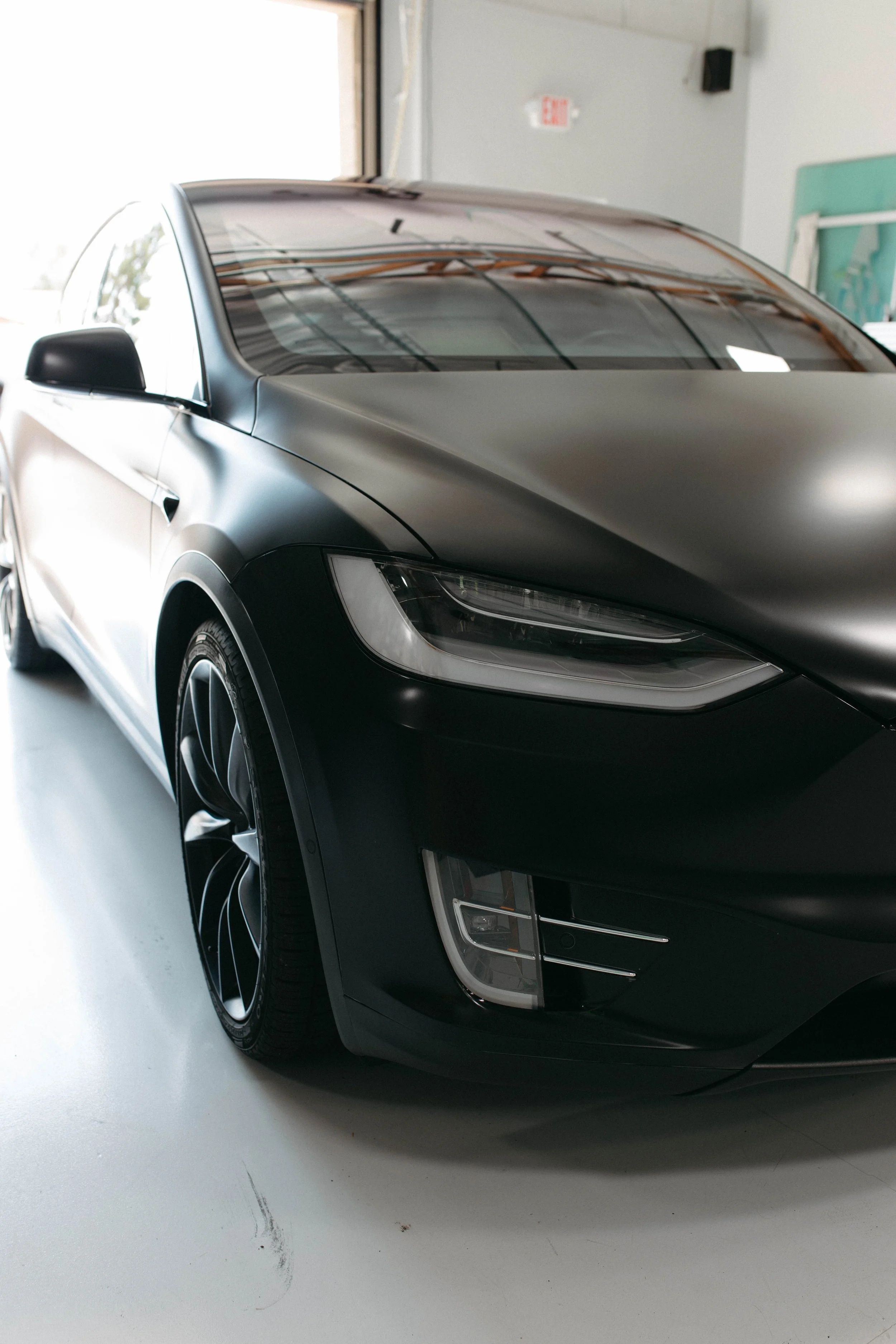 A black luxury car with sleek design, modern headlights, and stylish rims parked indoors near an open garage door.