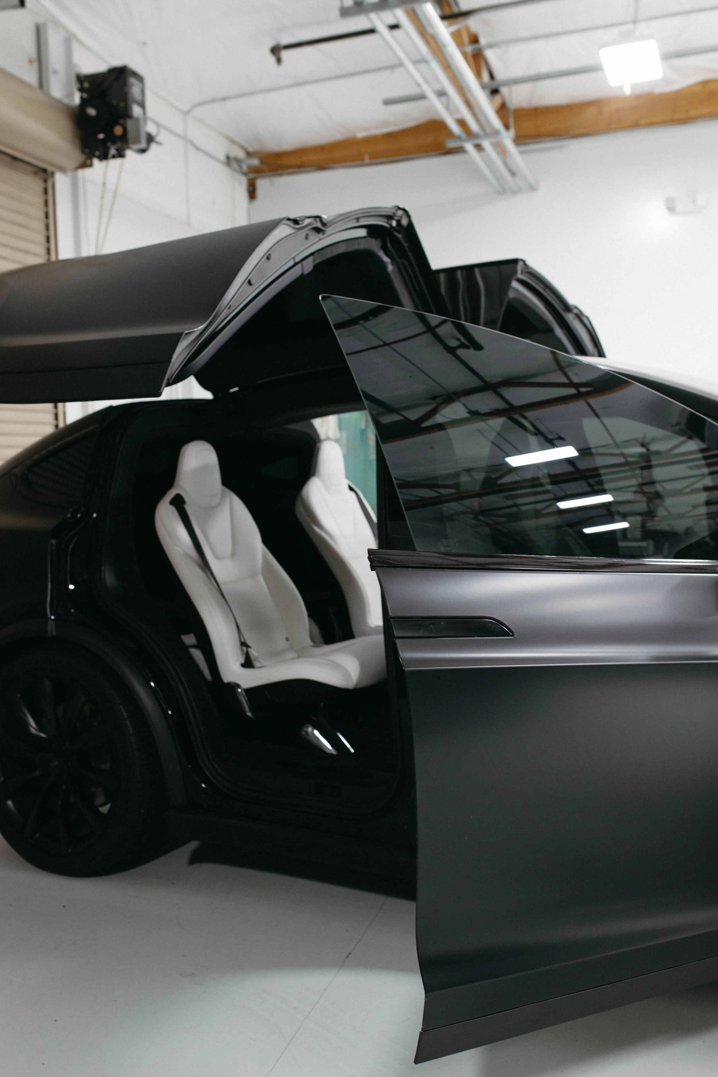 A Tesla Cybertruck with gull-wing doors open, showing white leather seats inside, parked inside a warehouse or garage.