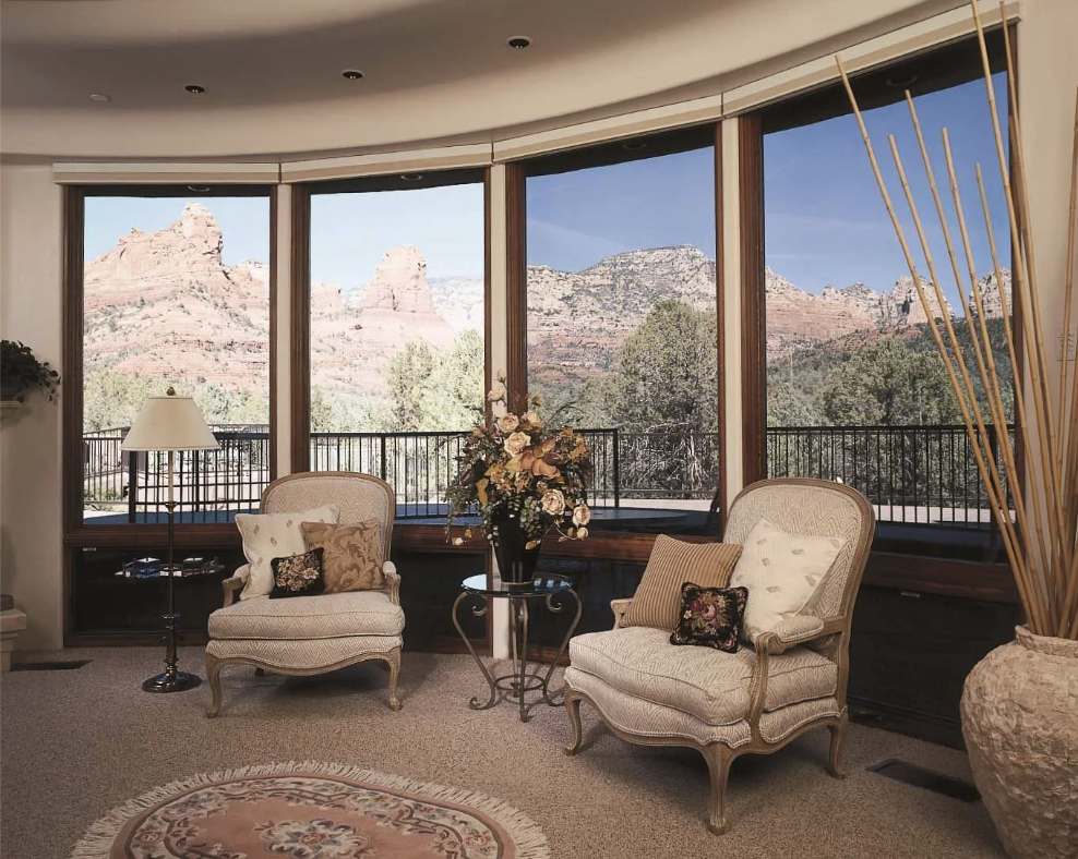 Living room with large window view of red rock mountains, two armchairs, a lamp, and a flower arrangement.
