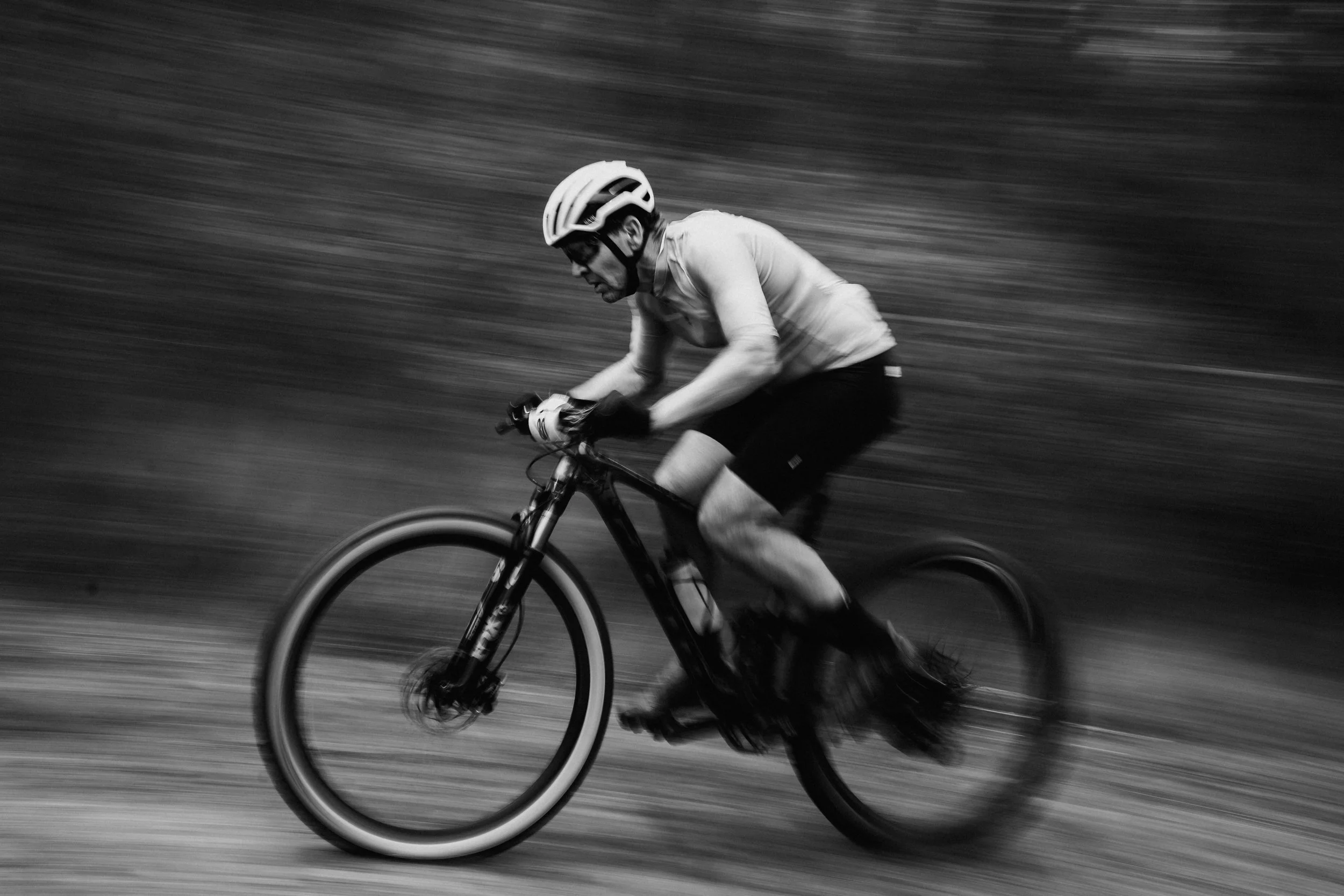 A man wearing a helmet and sports gear riding a mountain bike at high speed outdoors, with motion blur indicating fast movement.