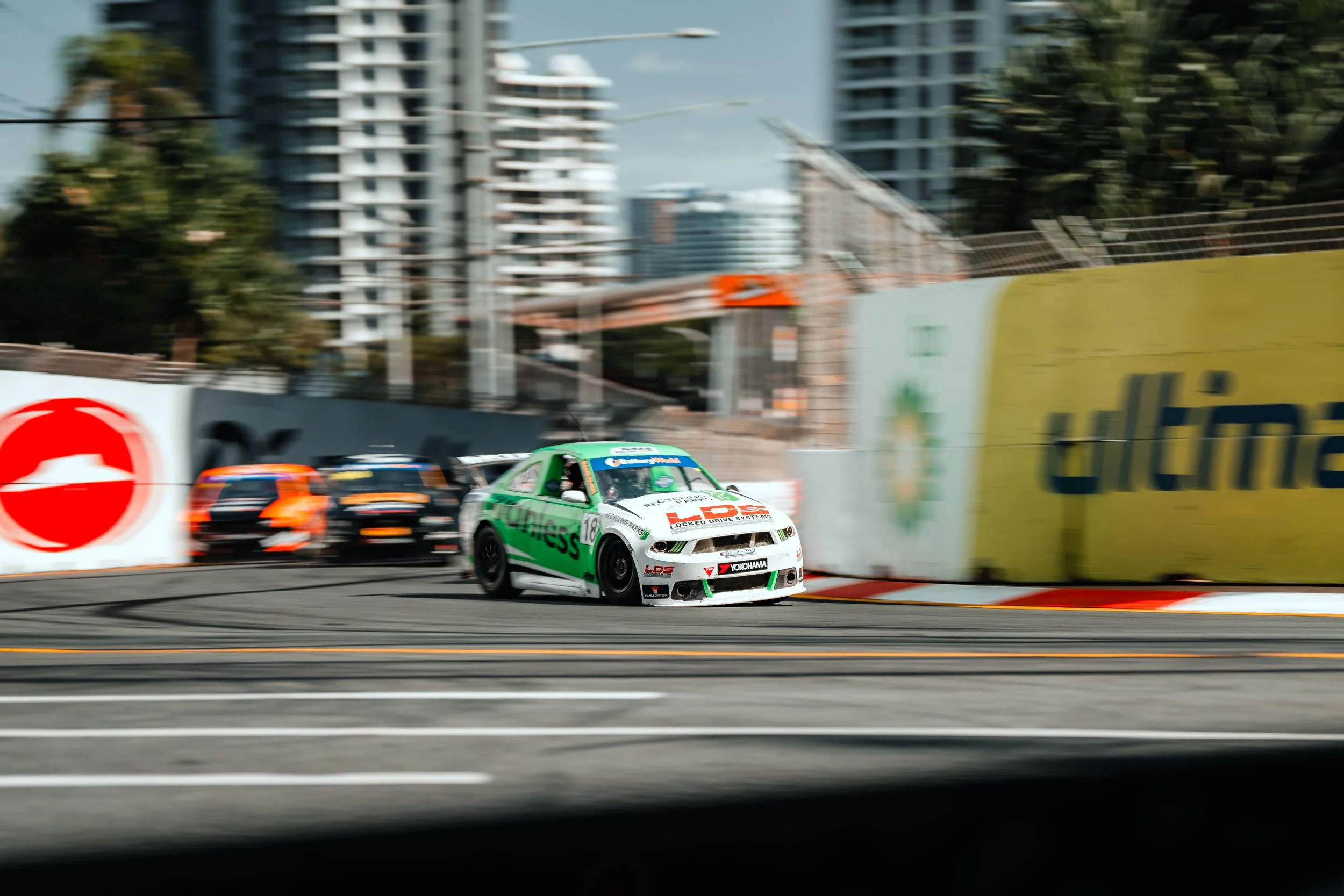 Race cars speeding on a city race track with buildings in the background.