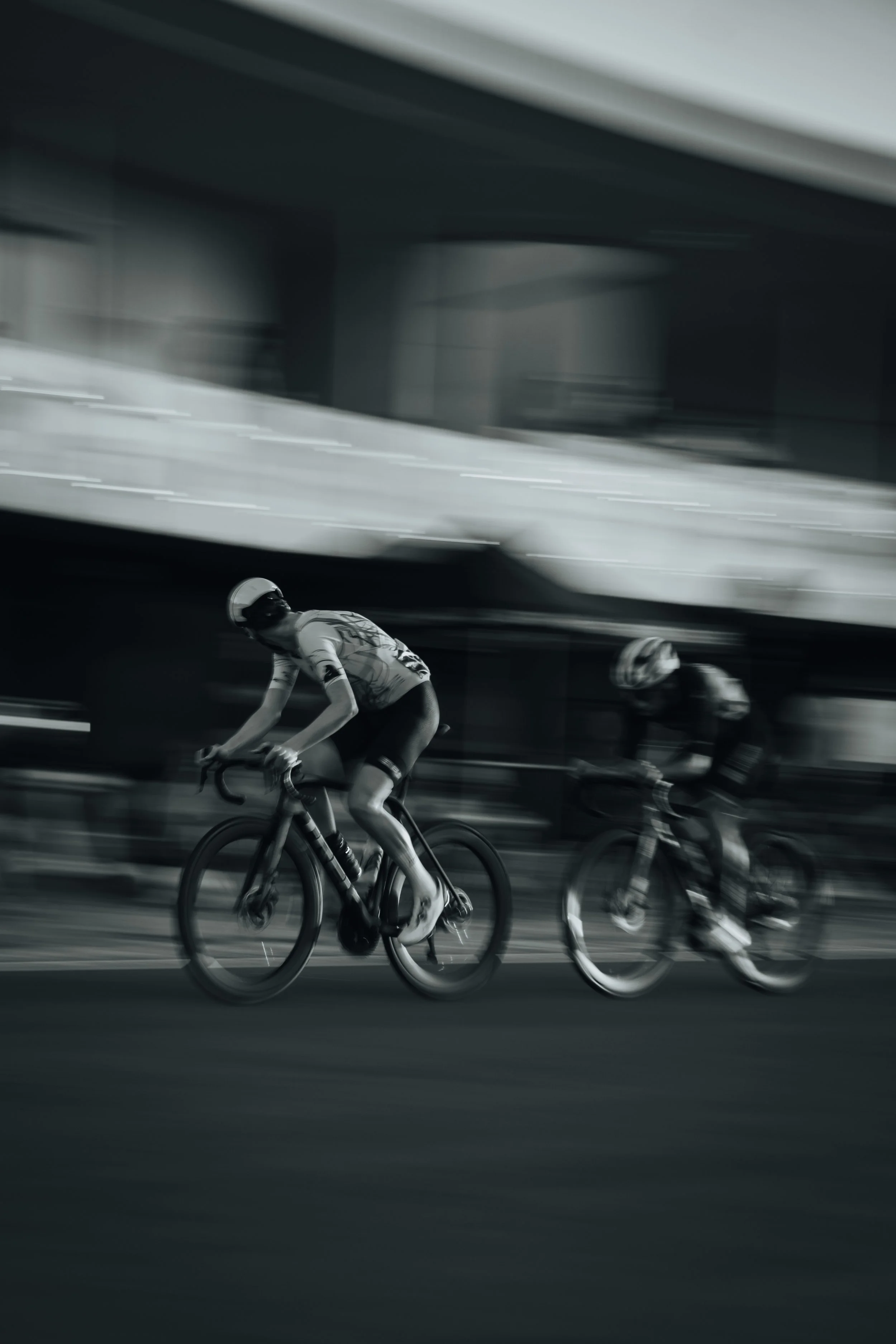 Two cyclists riding bicycles in a race under an overpass with motion blur.