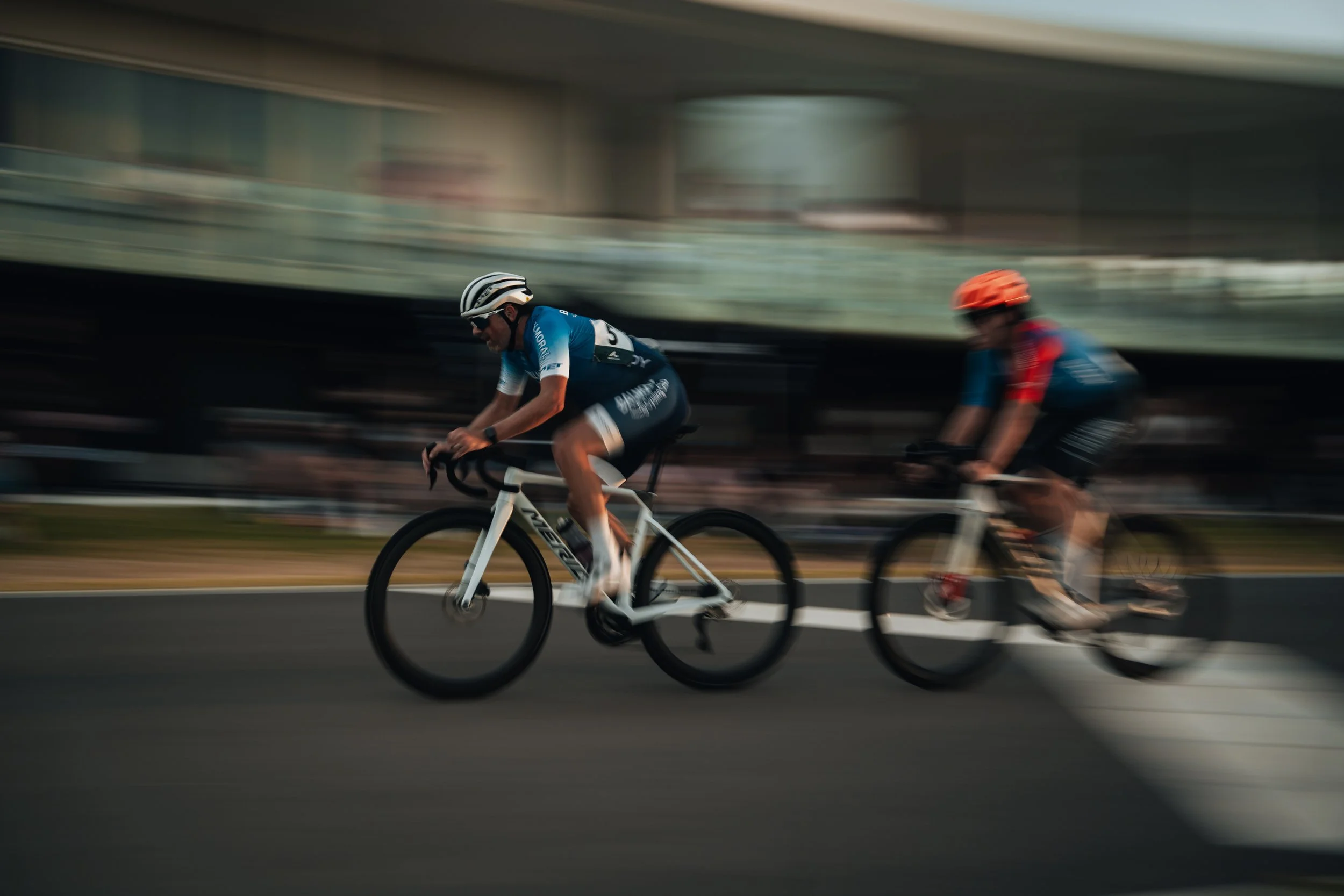 Two cyclists racing on a road during a competitive event, with a blurred background indicating motion.
