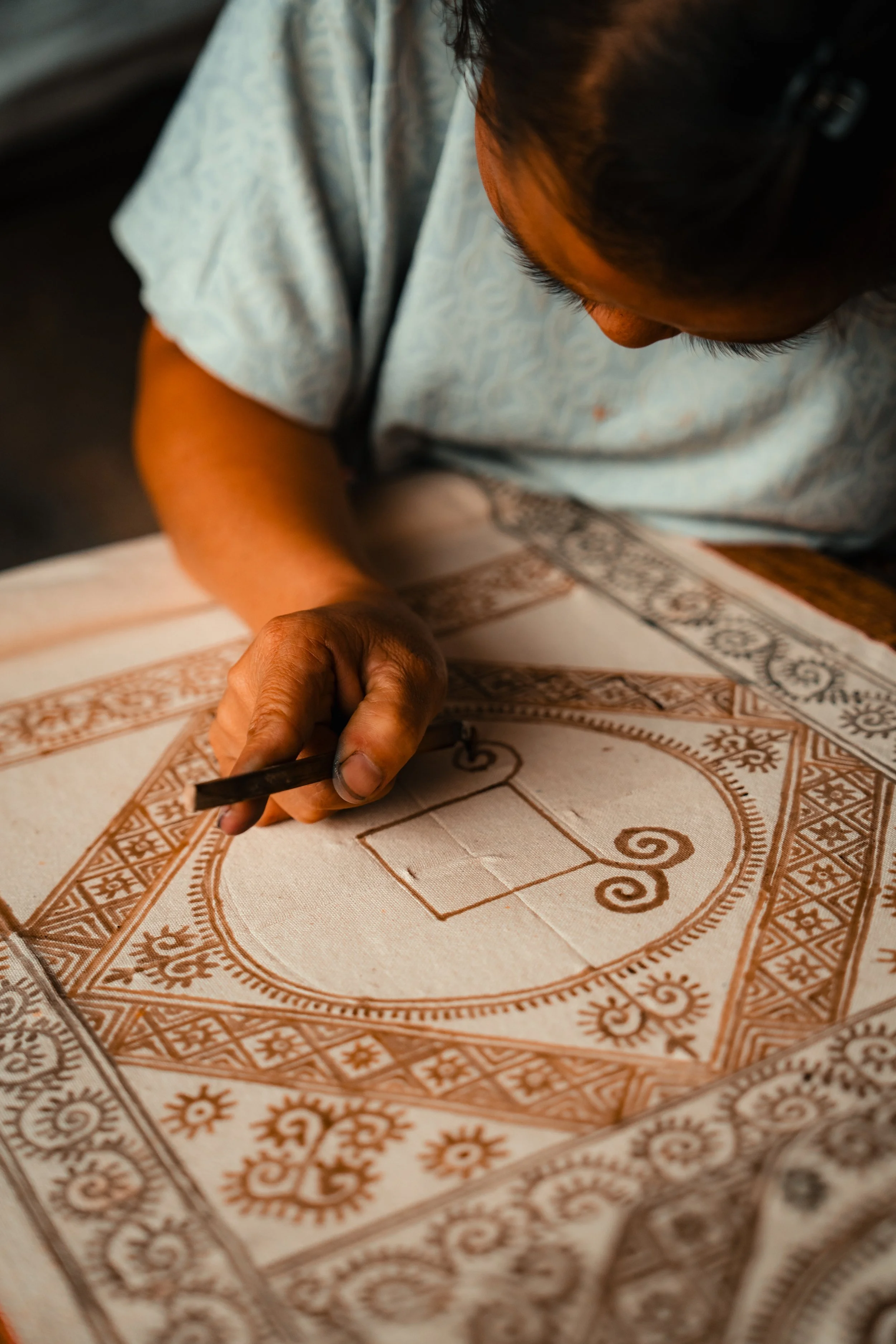 Person drawing a geometric pattern or design on fabric with a tool.