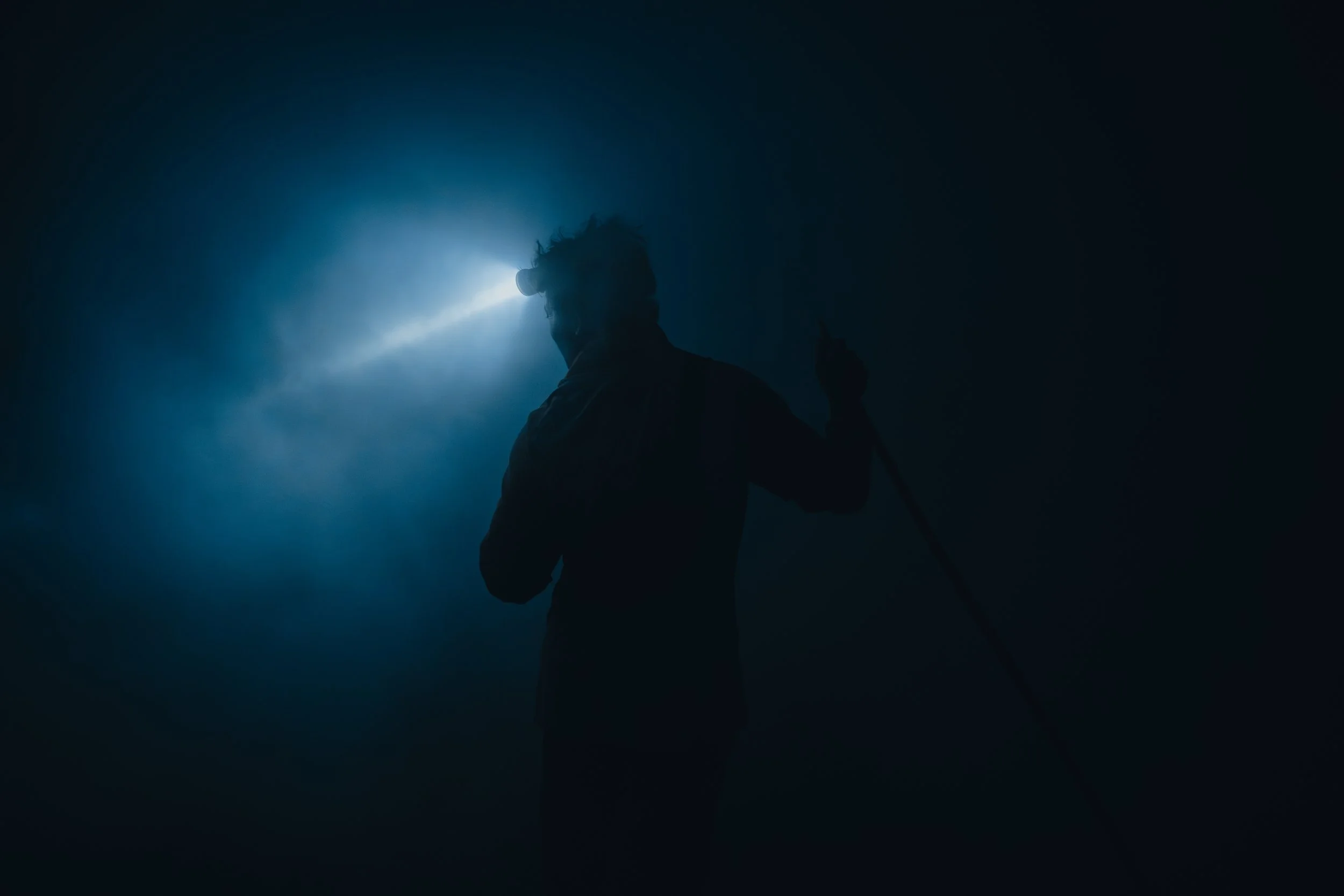 A silhouette of a person holding a walking stick or cane against a dark background with a bright light shining behind their head.