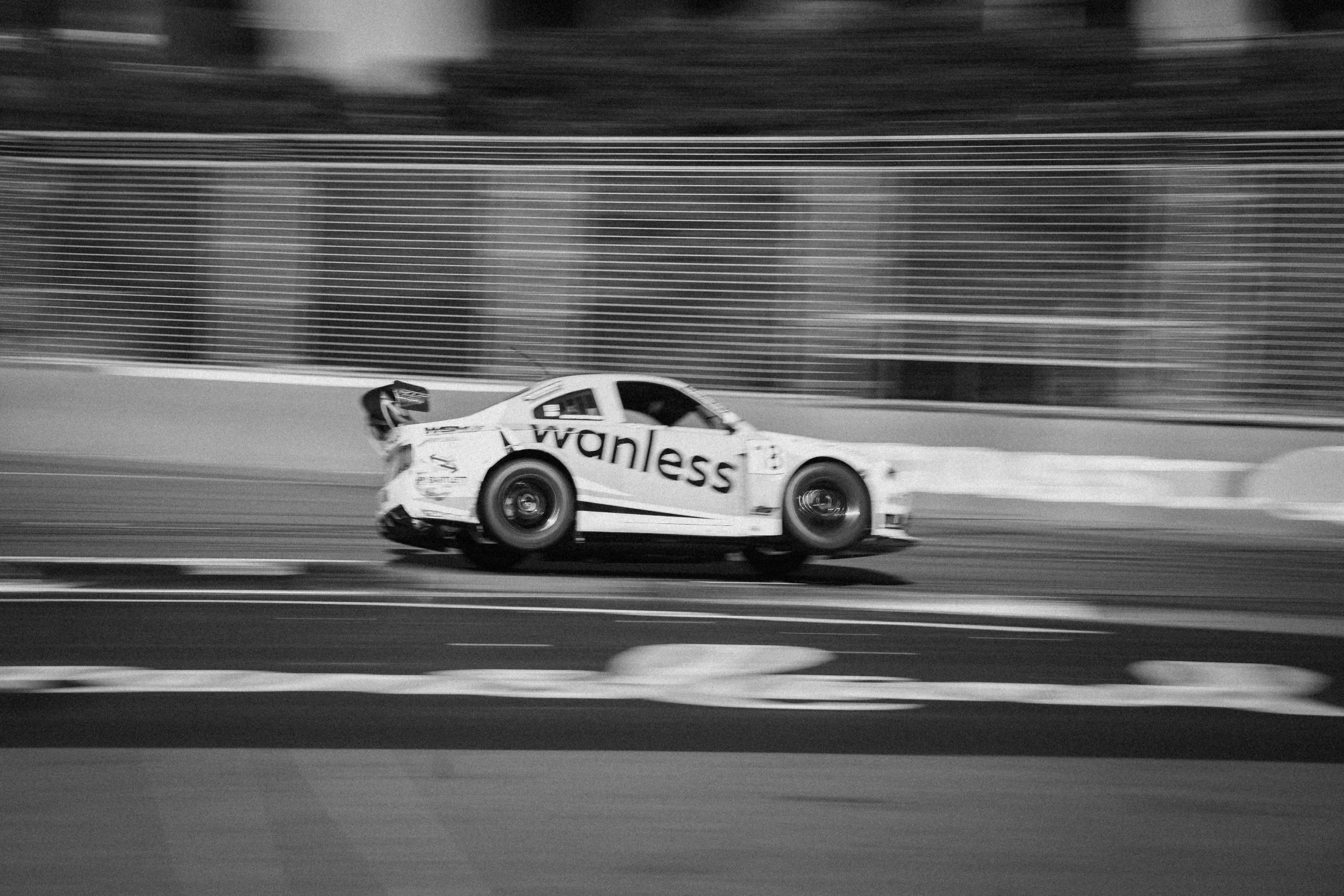 Black and white photo of a racing car on a track, with motion blur in the background.