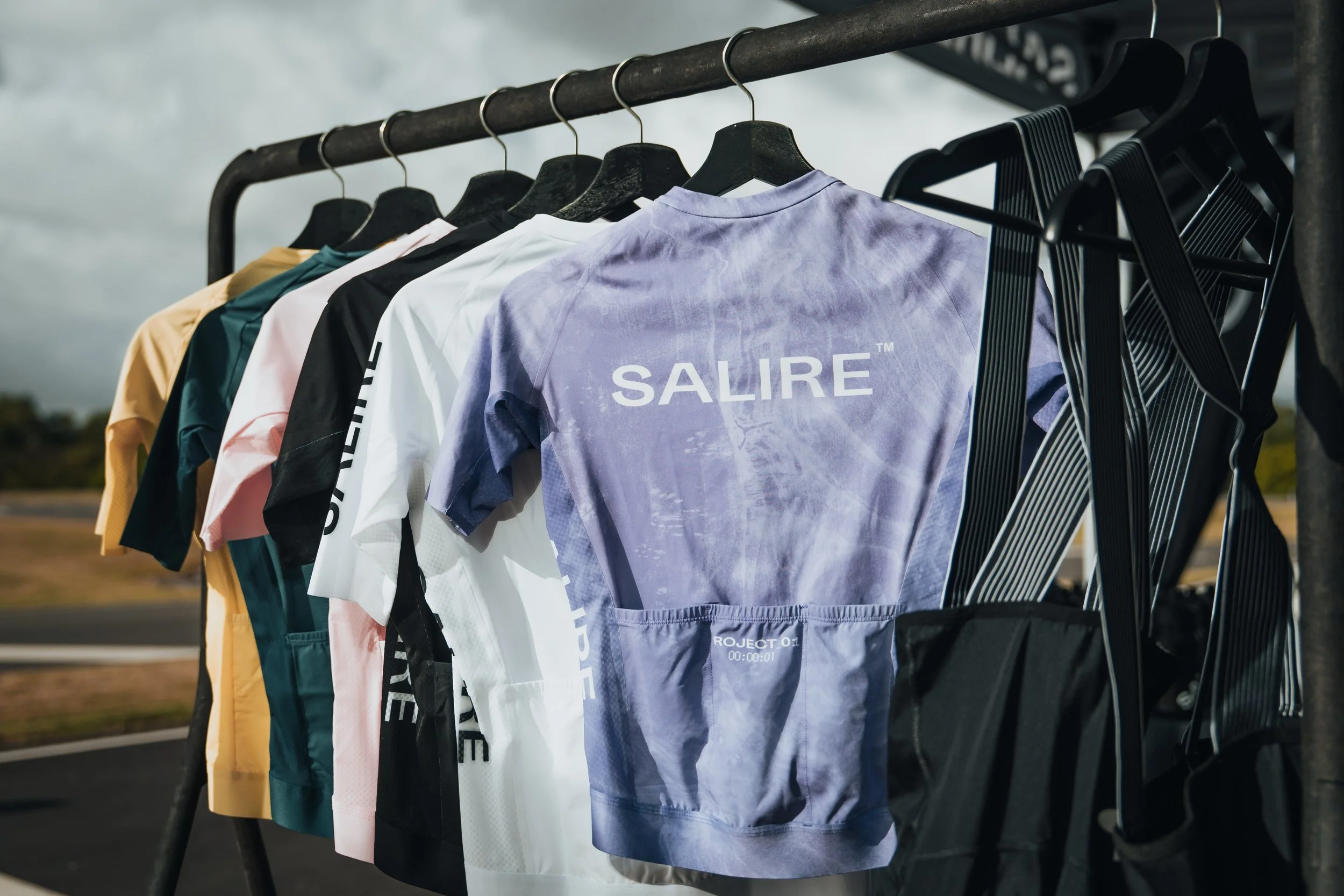 A rack of colorful athletic shirts and accessories hanging outdoors on a cloudy day.