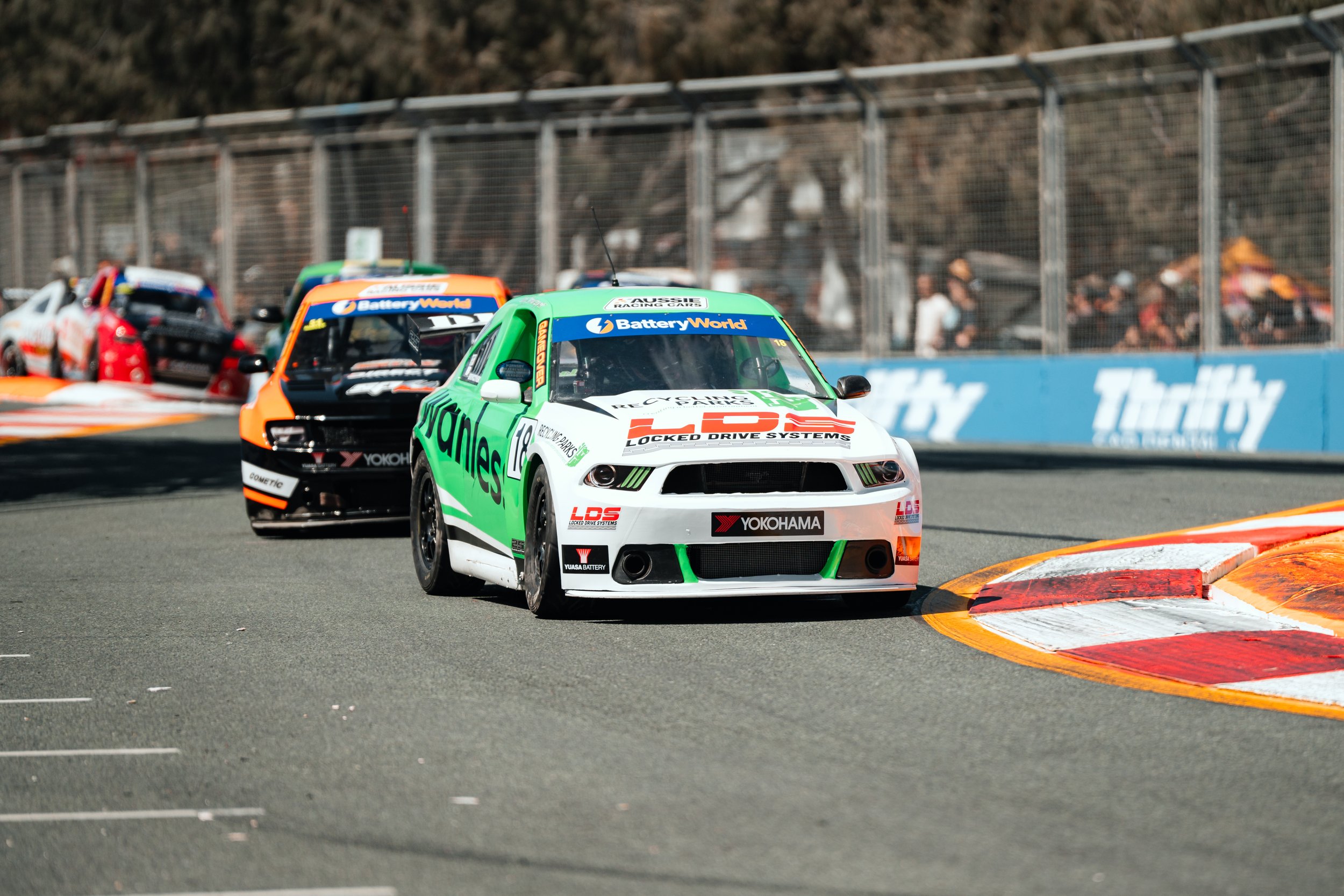 Race cars on a track during a race, with colorful liveries and sponsor decals, navigating a sharp turn.