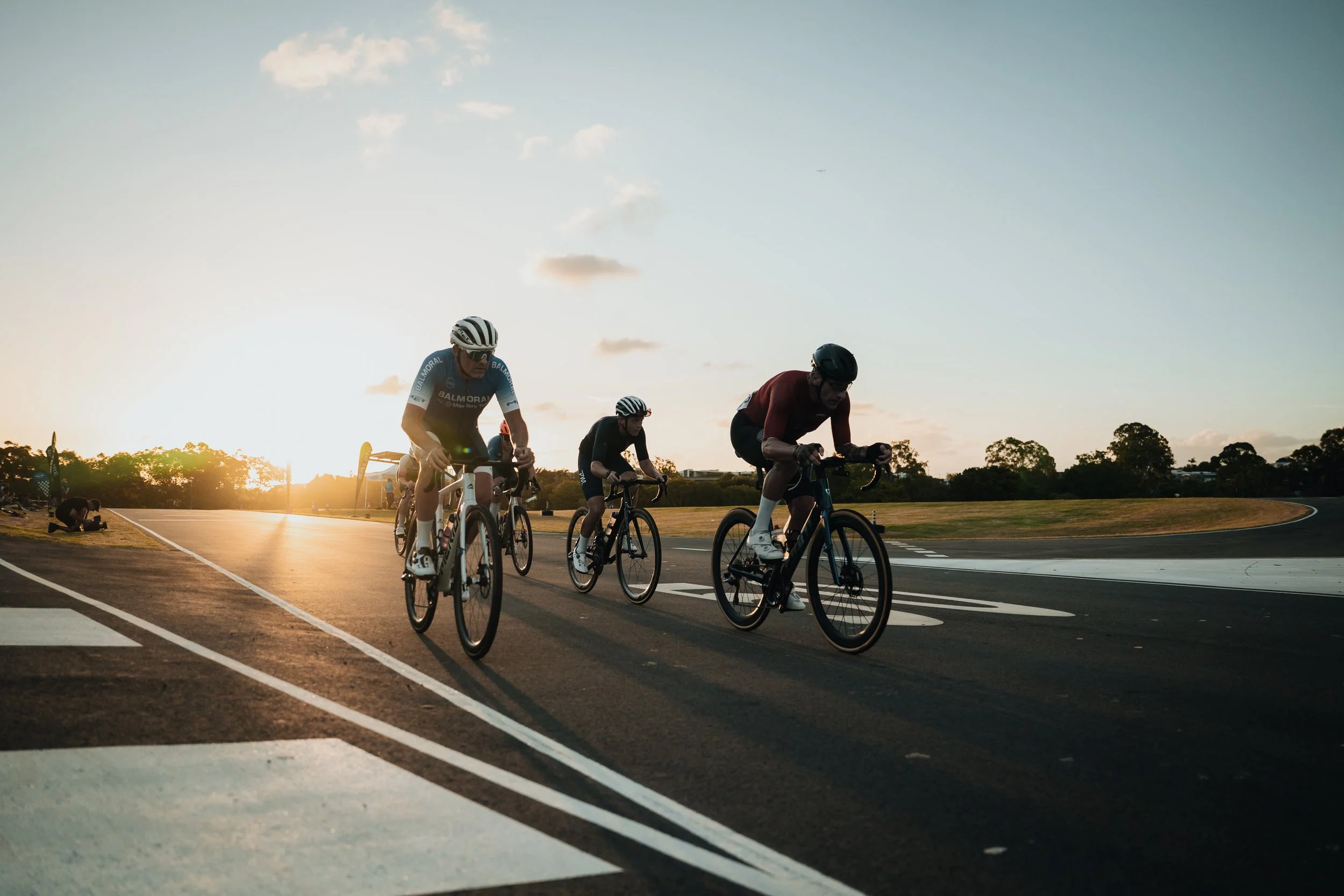 Cyclists riding on a paved track at sunset.