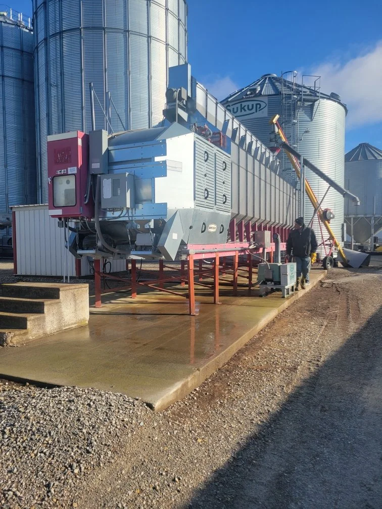 Large grain storage silos with a grain dryer in a farm setting.