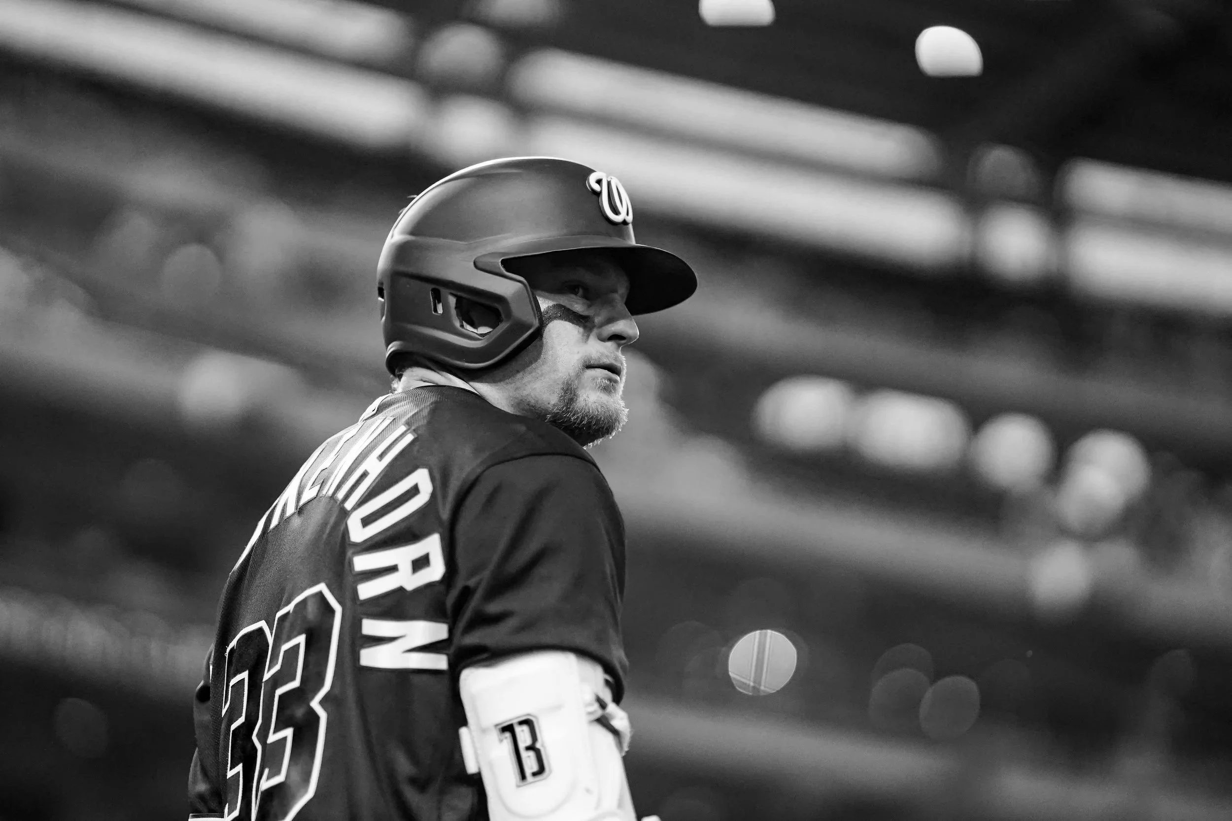 Black and white photo of a baseball player wearing a helmet and jersey, looking to the side in a stadium.