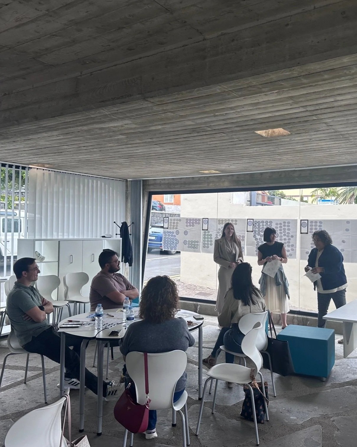 Group of people in a modern conference room with large windows and natural light. Three women are standing near the window, presenting about ecotourism in the Canary Islands. They are specifically talking about wine tourism opportunities in Tenerife.