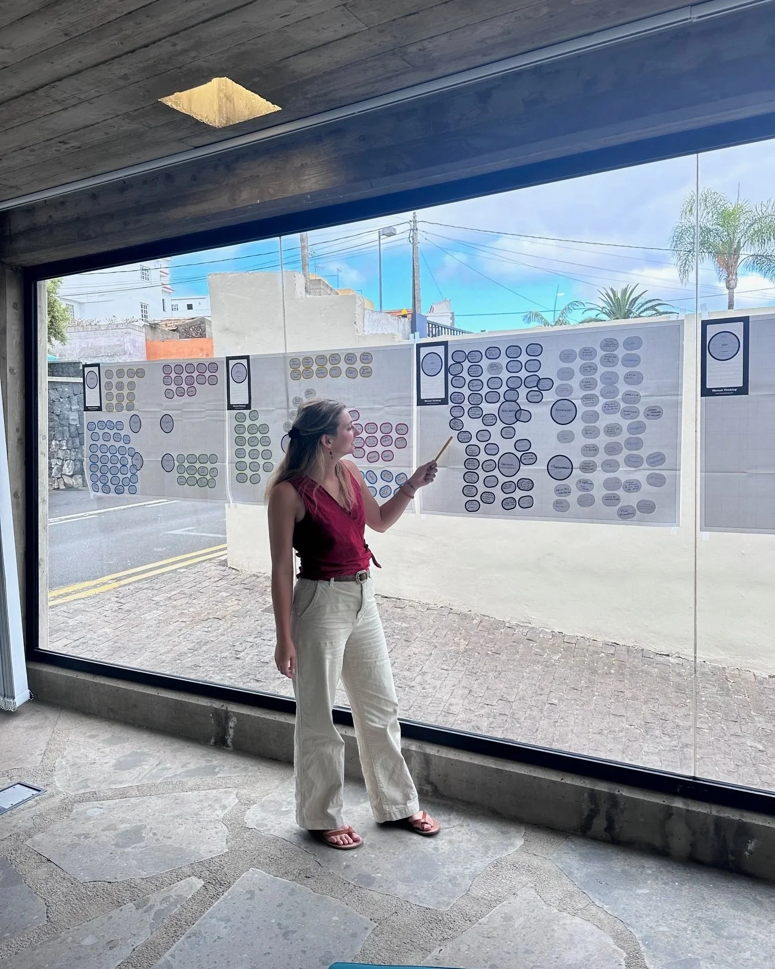 A woman wearing a red top and cream-colored pants giving a presentation about sustainable tourism. She is explaining her "brainstorming" exercise that focused on public private partnerships in the Canary Island wine tourism space.