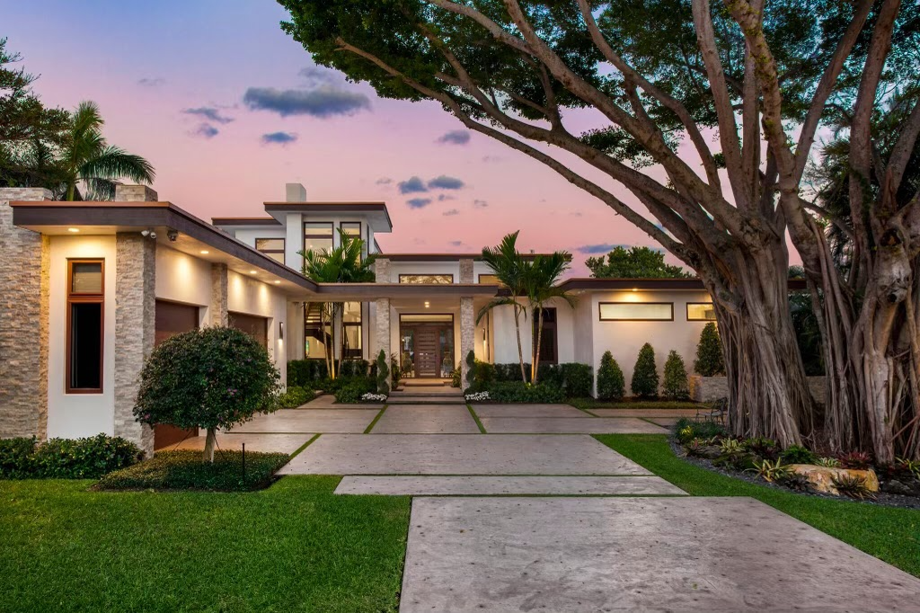 Modern house with large tree in front, well-maintained lawn, and landscaped plants, at sunset