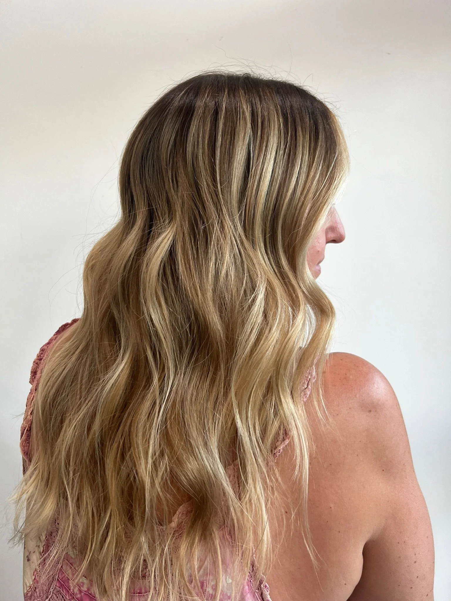A woman with wavy blonde hair is shown from the side against a plain background.