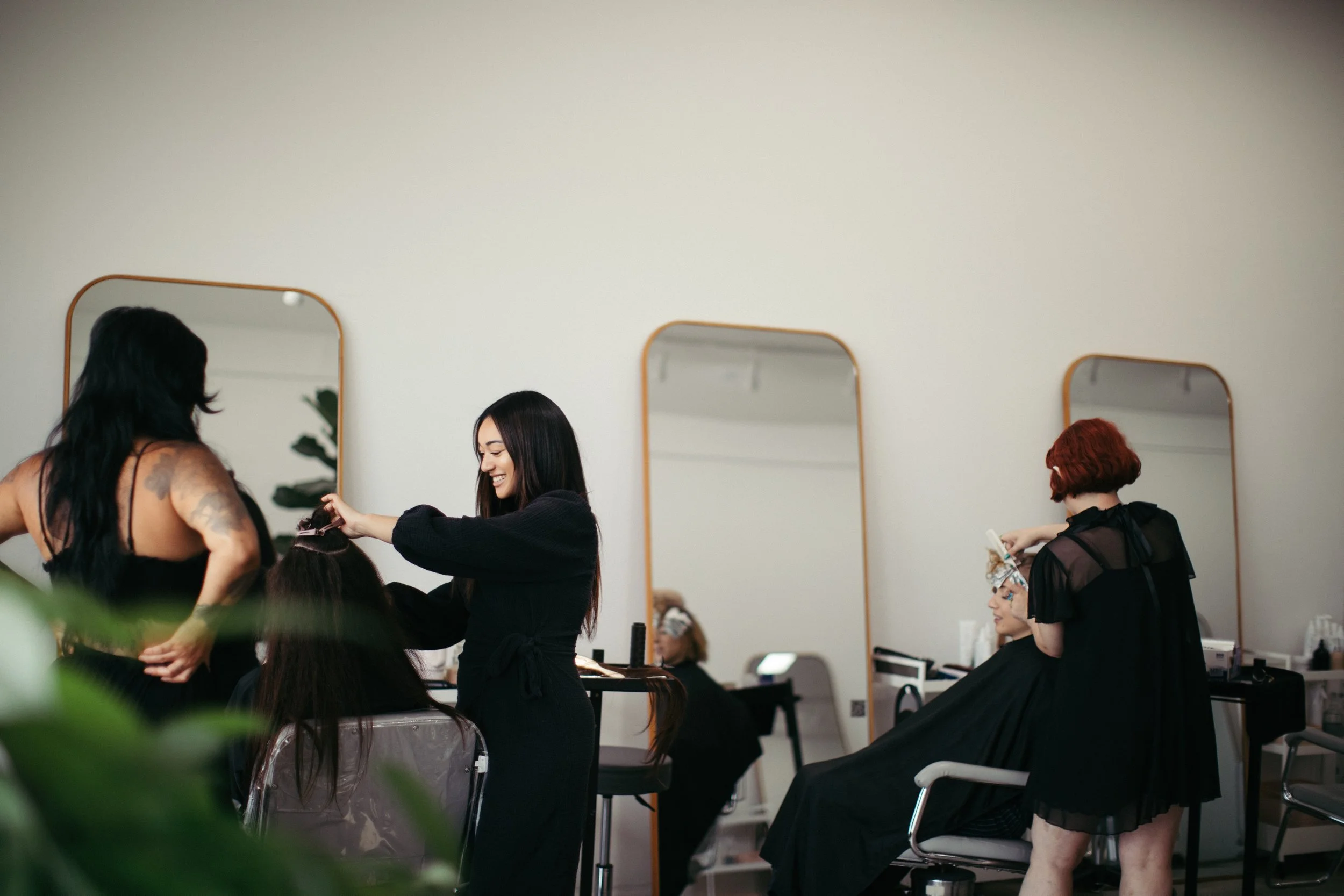 Women receiving hair styling services in a salon with large mirrors and styling tools.