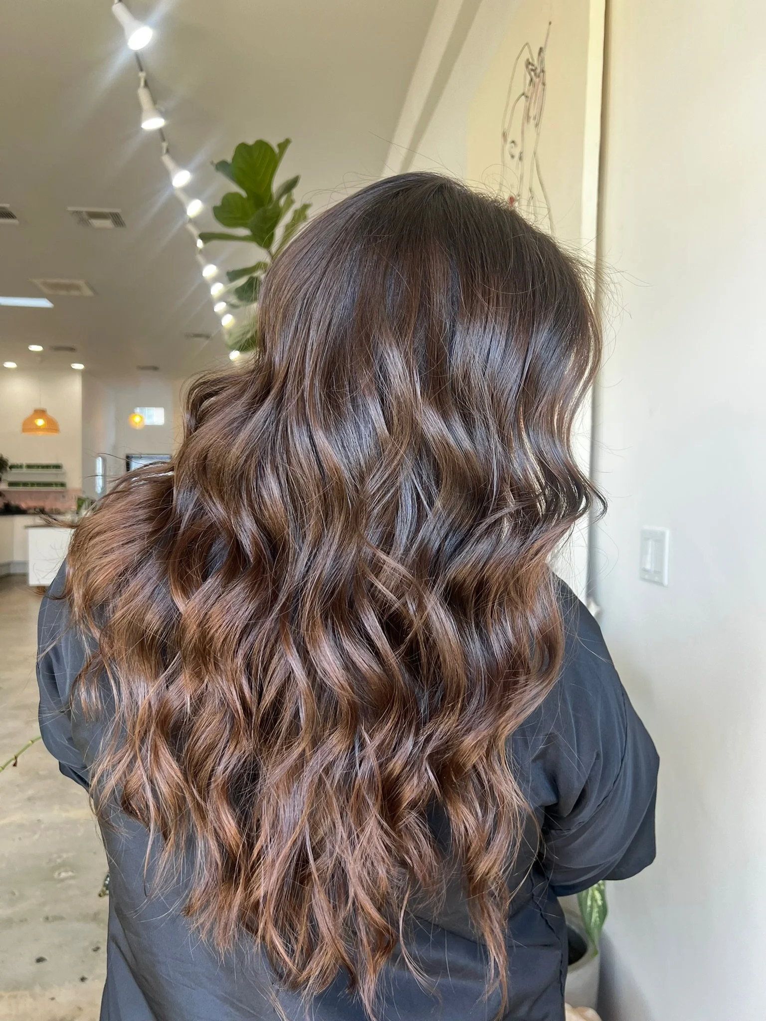 A woman with long, wavy brown hair inside a hair salon.