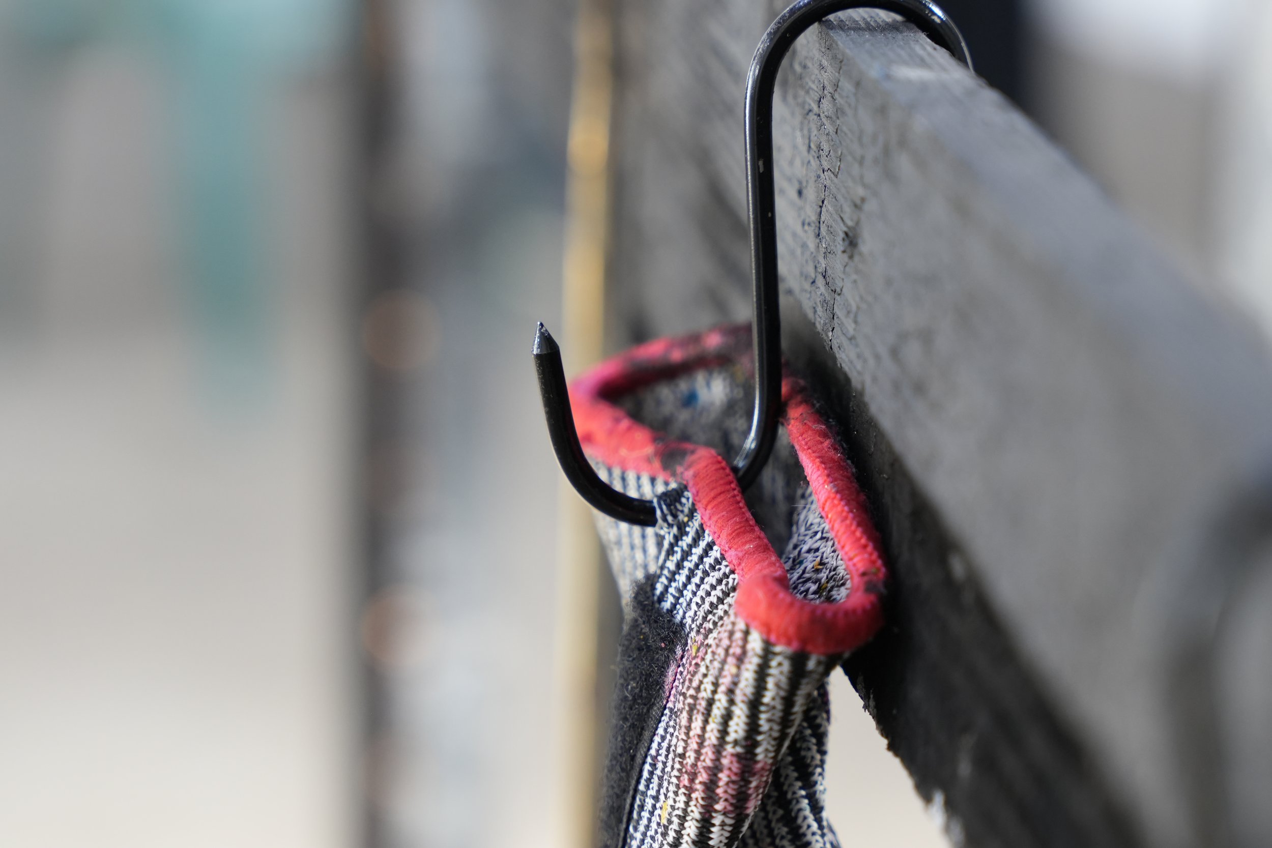 A black hook with a pointed end holding a plaid cloth with red edges against a blurred background.