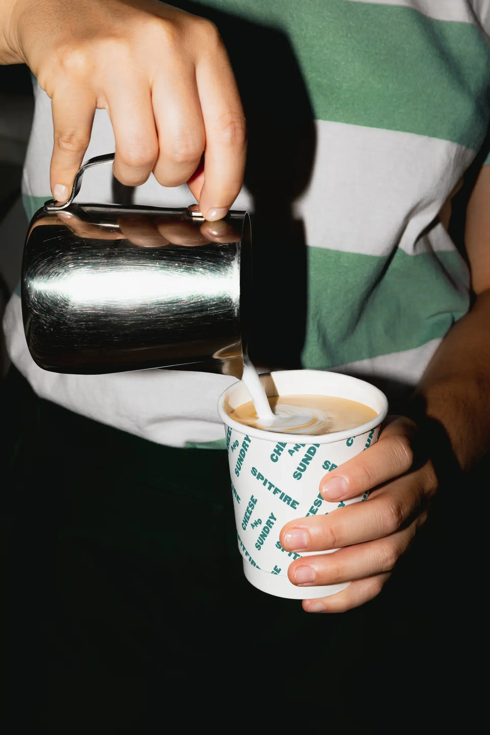 Person pouring cream into a Spitfire coffee cup from a metallic pitcher.