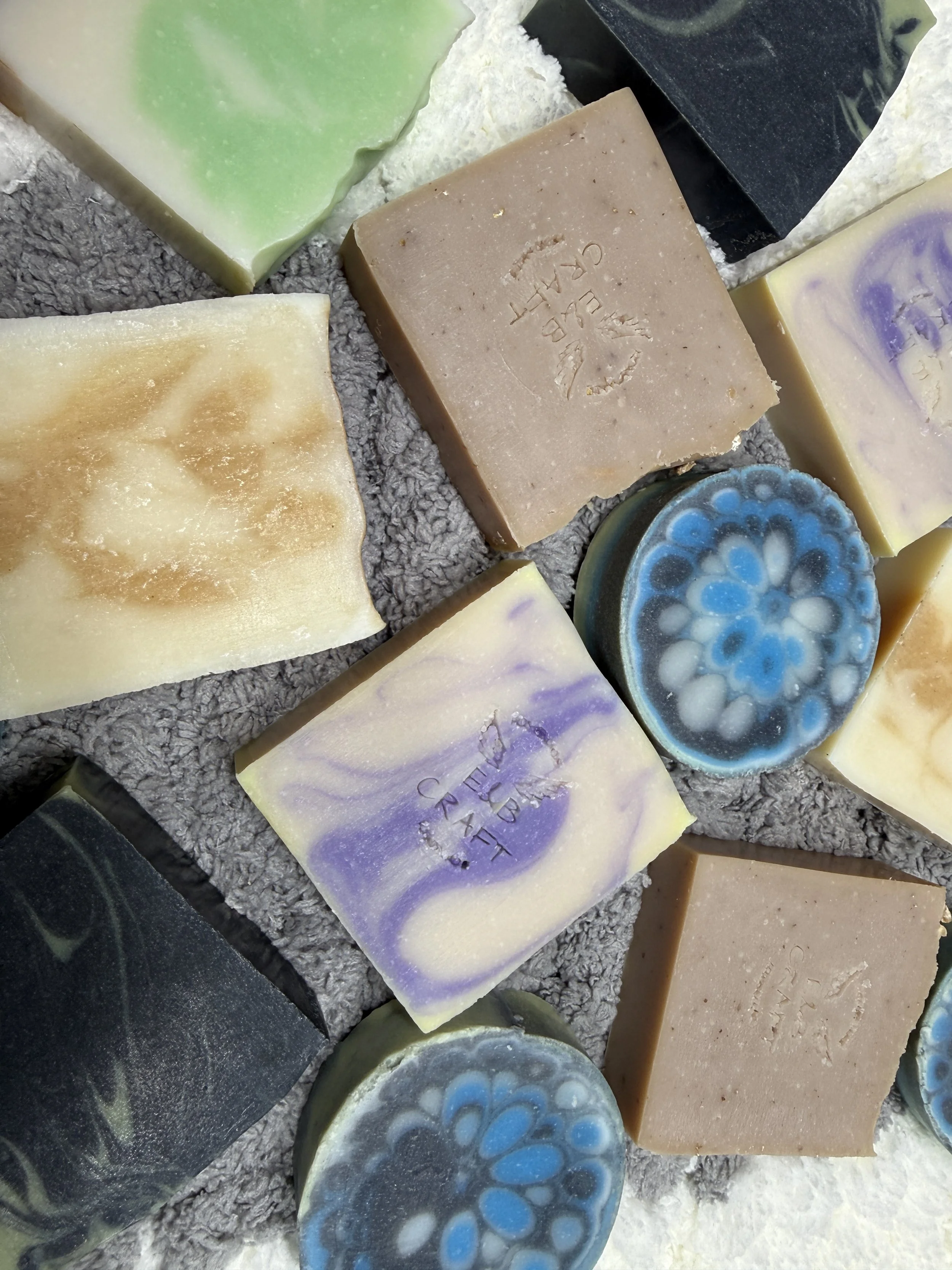 Assorted handmade soap bars of various colors and designs on a gray textured surface.