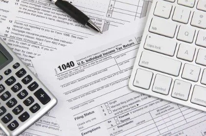Tax form 1040, calculator, pen, and keyboard on a desk.