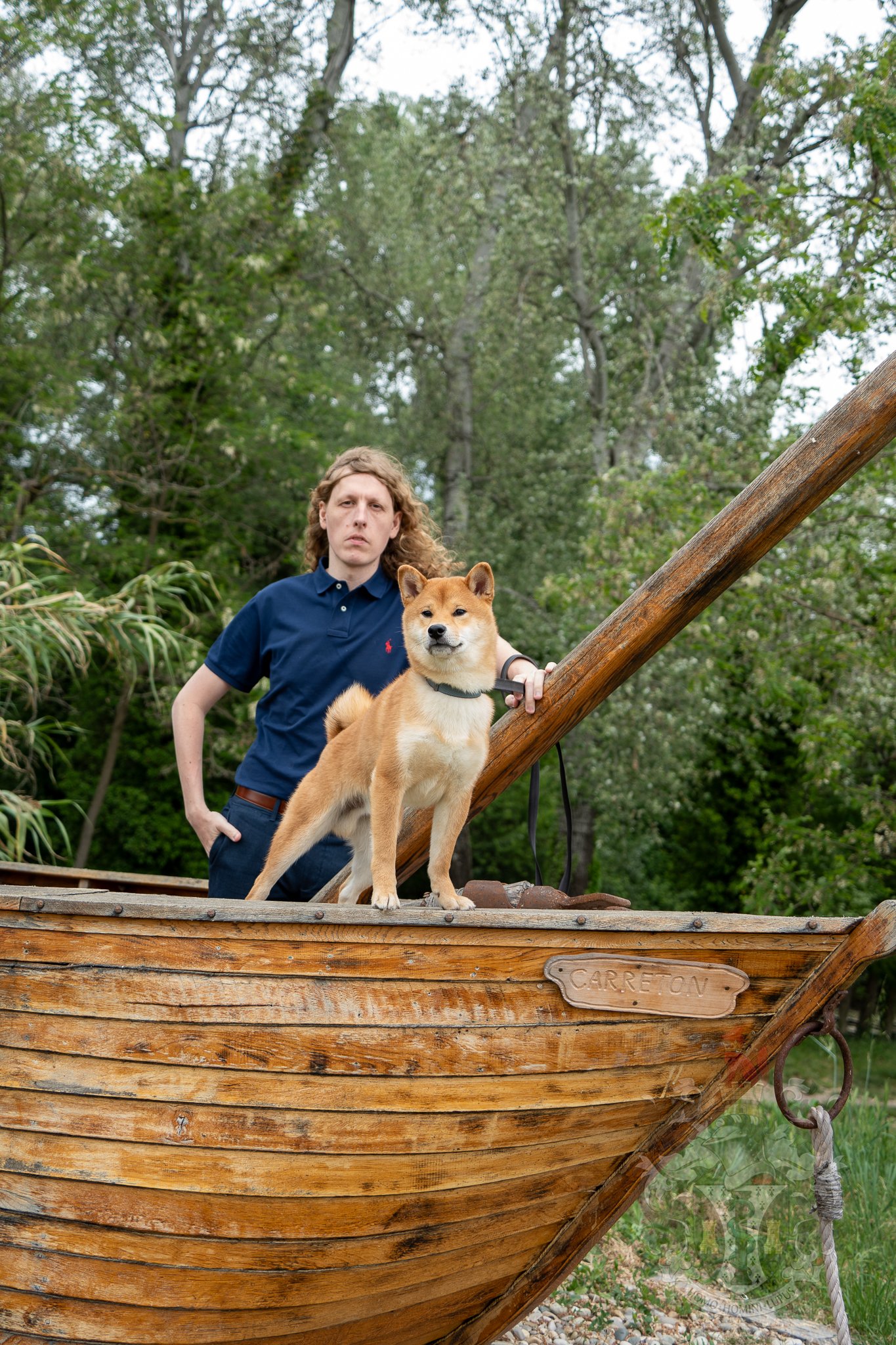 Red Shiba Inu Ace sitting attentively by a wooden boat near a stream in L'Homme d'Armes, Isère.