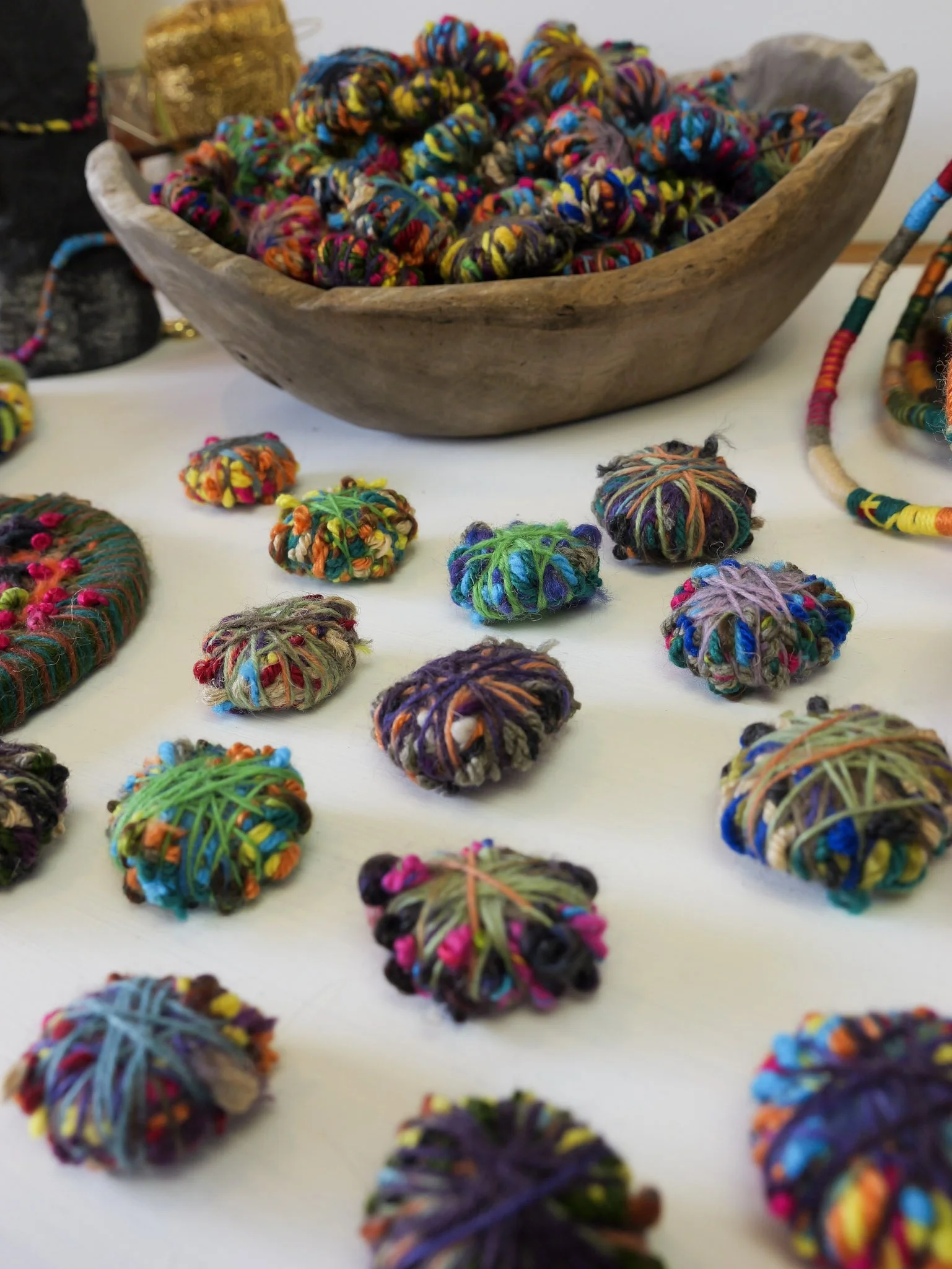 Colorful yarn balls and twisted skeins arranged on a white surface with a large wooden bowl filled with multicolored yarn in the background.