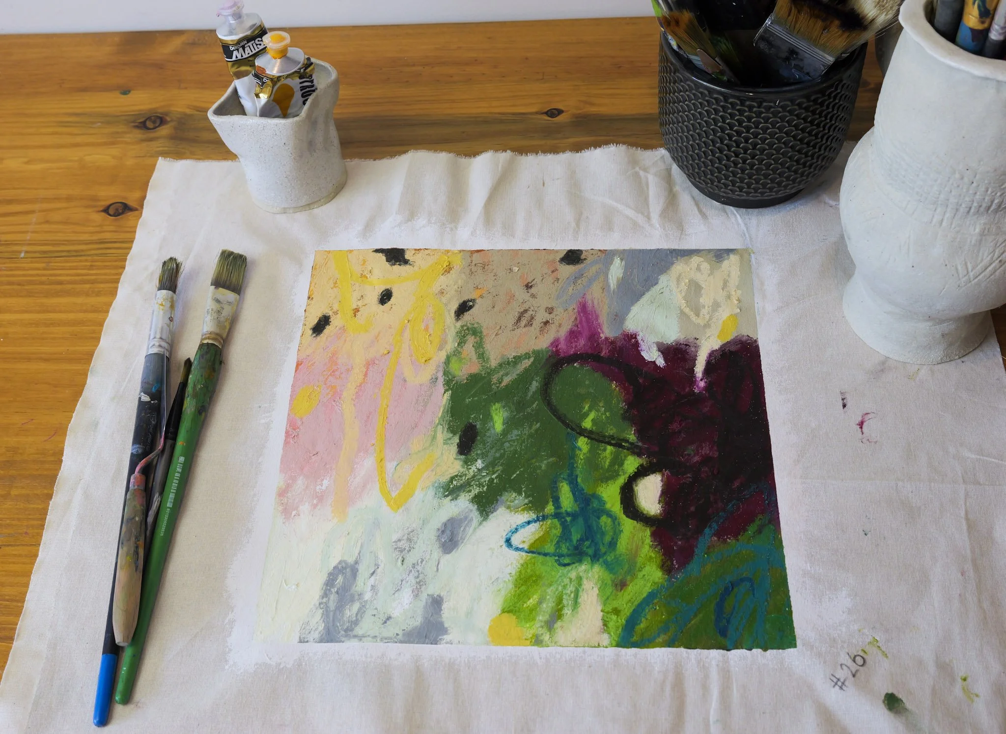 Colorful abstract painting on a canvas, surrounded by paintbrushes, and art supplies on a wooden table.