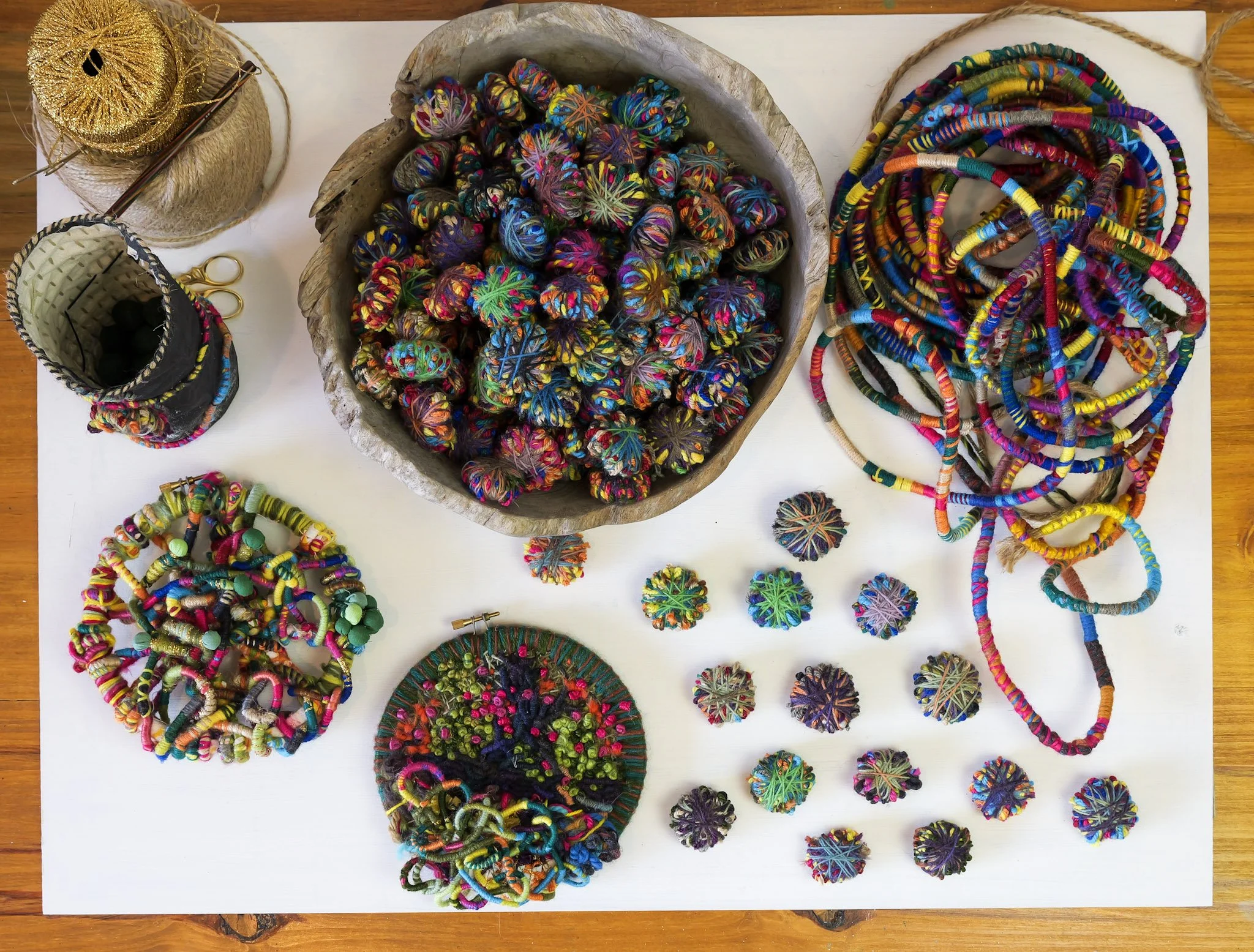 Colorful handwoven jewelry and accessories includes necklaces, bracelets, and pins with intricate patterns and vibrant colors displayed on a white surface.