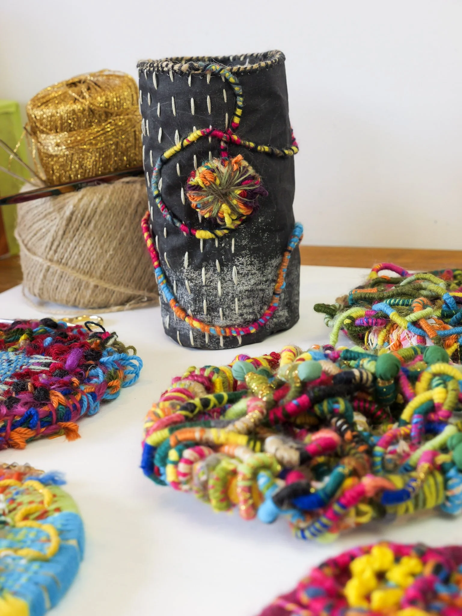 Colorful handmade jewelry displayed on a table, including bracelets and necklaces, with a decorated black container and fabric in the background.